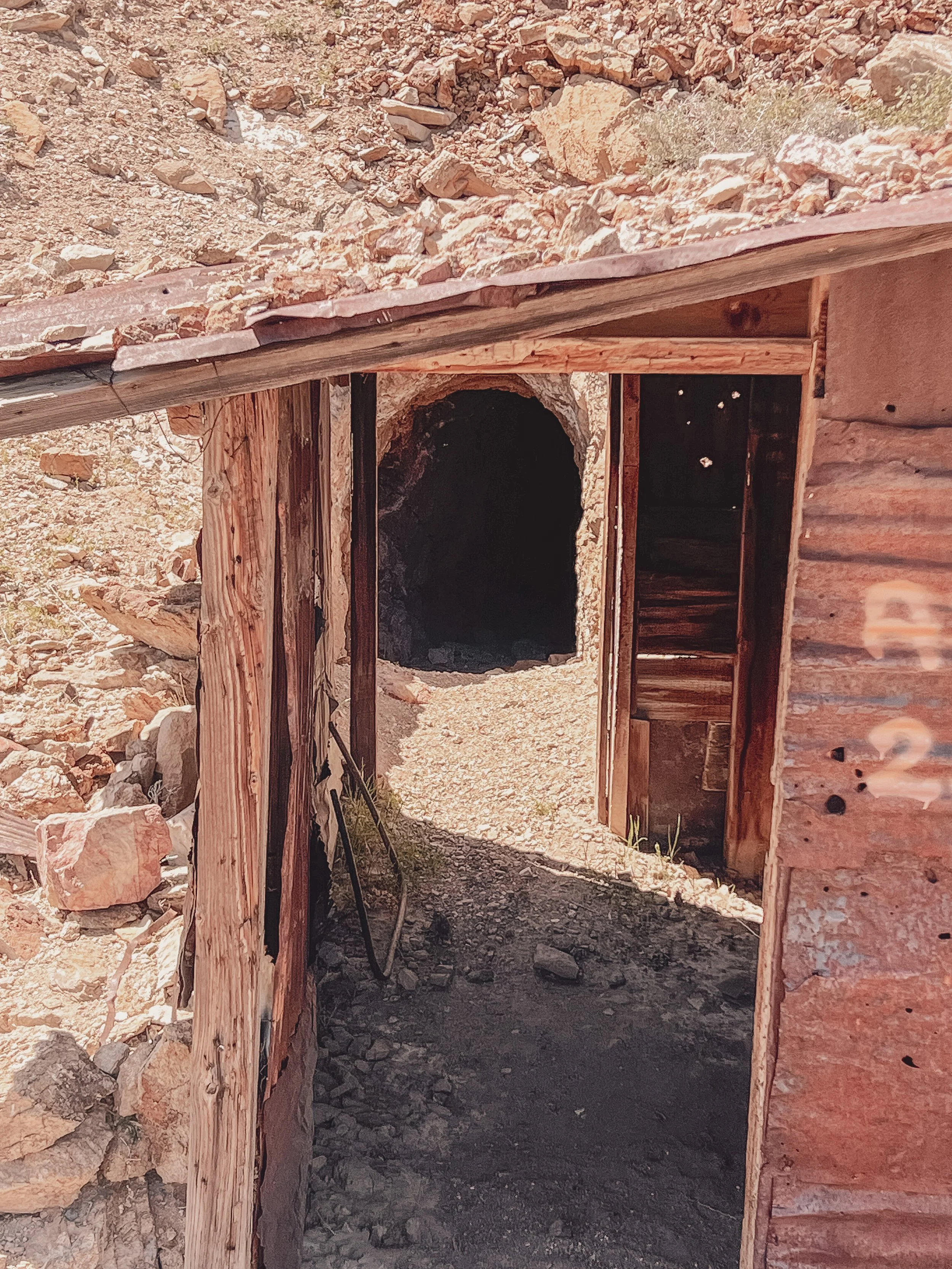 Old wooden structure with a dark tunnel or cave opening in the background, surrounded by rocks and dirt.