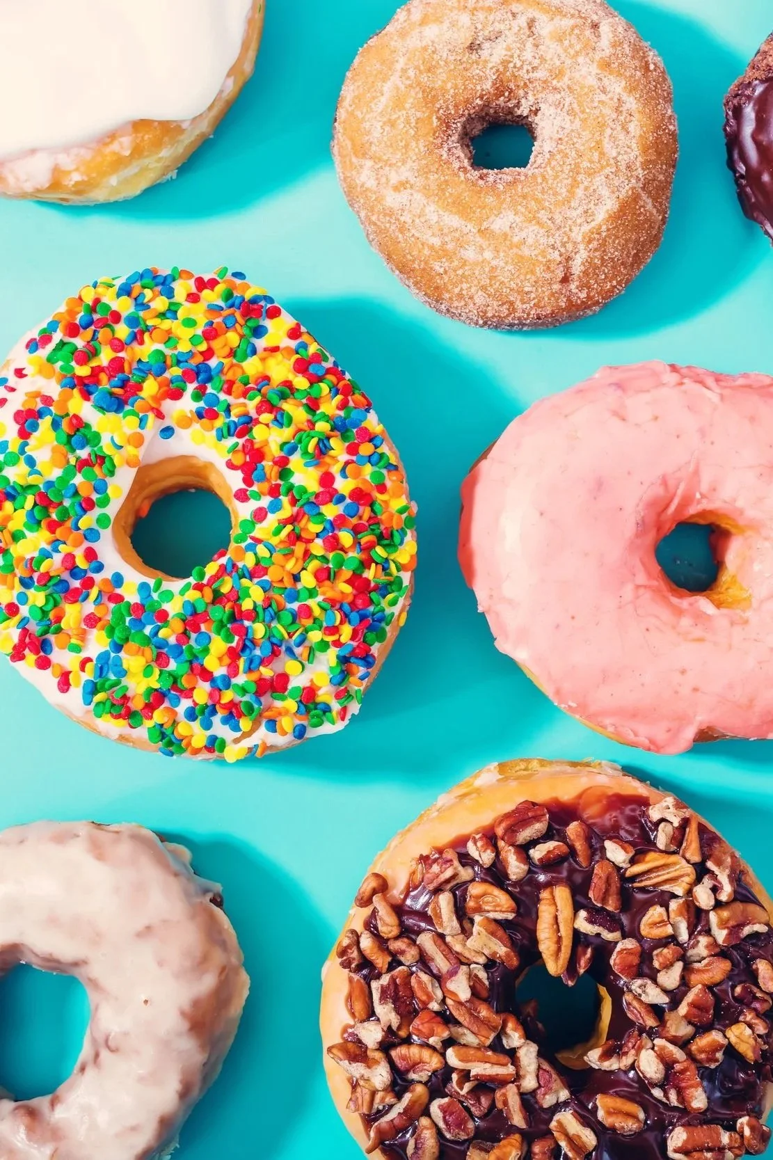 Colorful assortment of donuts with various toppings on a bright blue background.