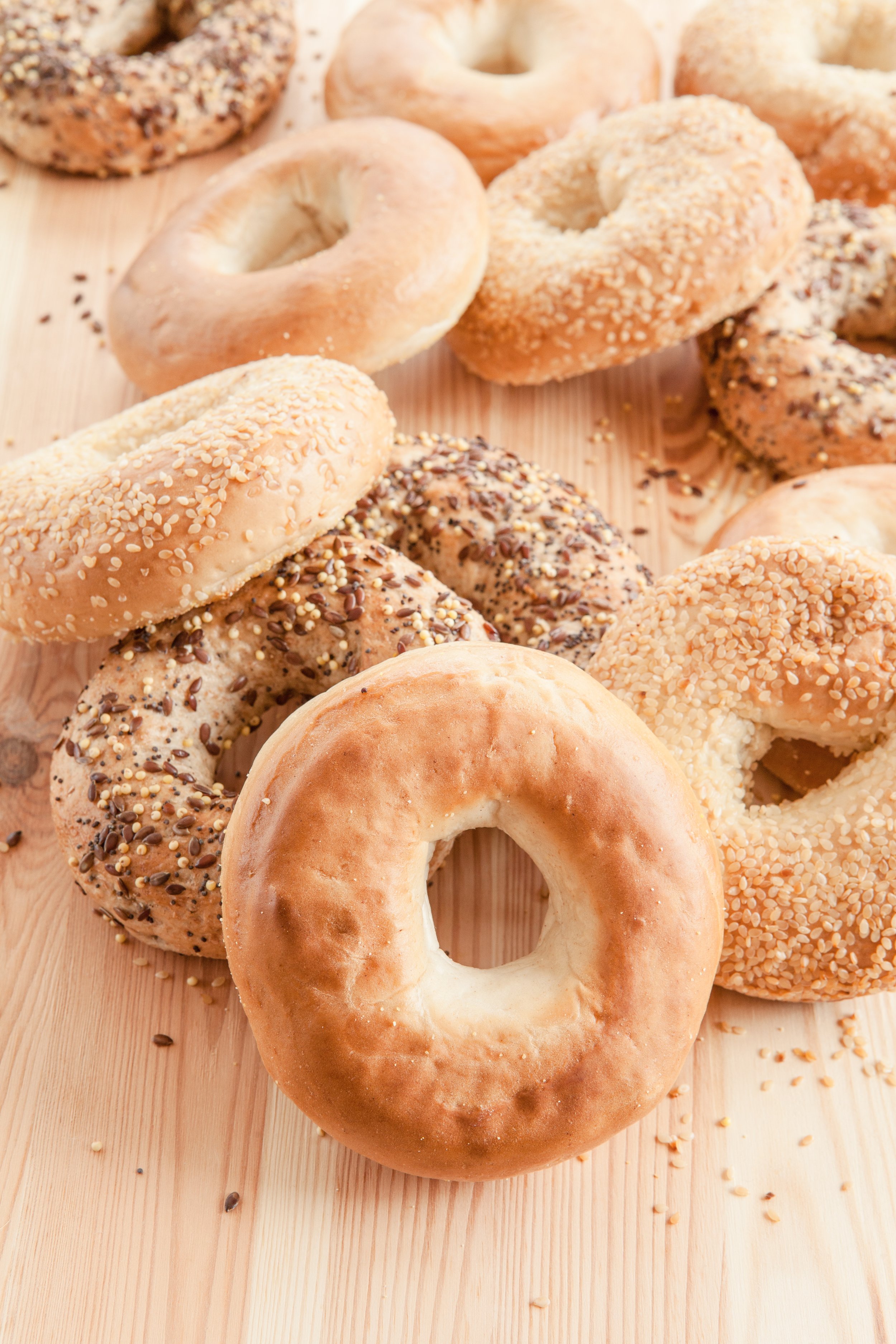 Assorted bagels on a wooden surface, some topped with sesame or other seeds.