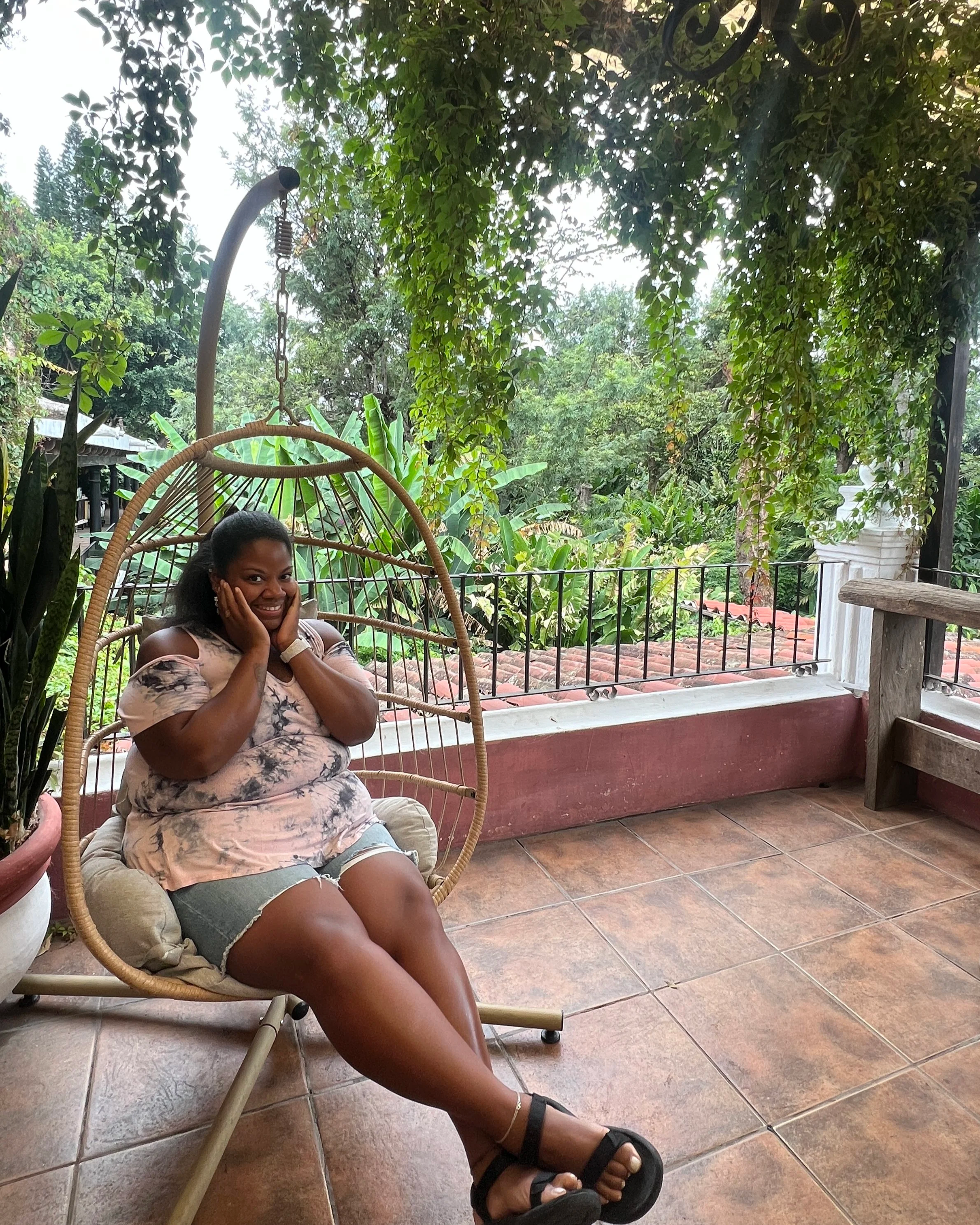 Lissette in a garden holding her face in a straw swing