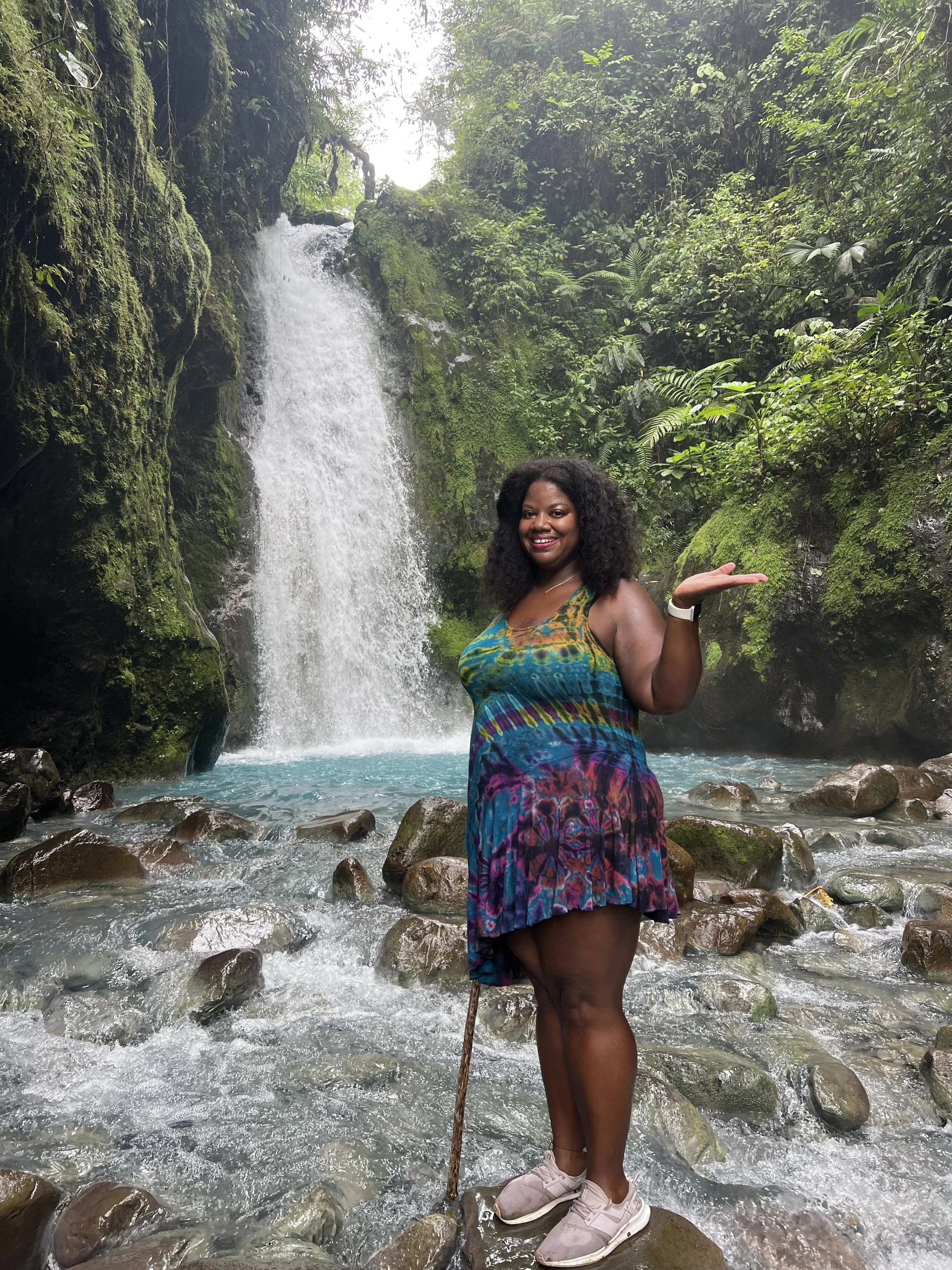 Portrait of Lissette in a tie dye dress standing in front of a waterfall
