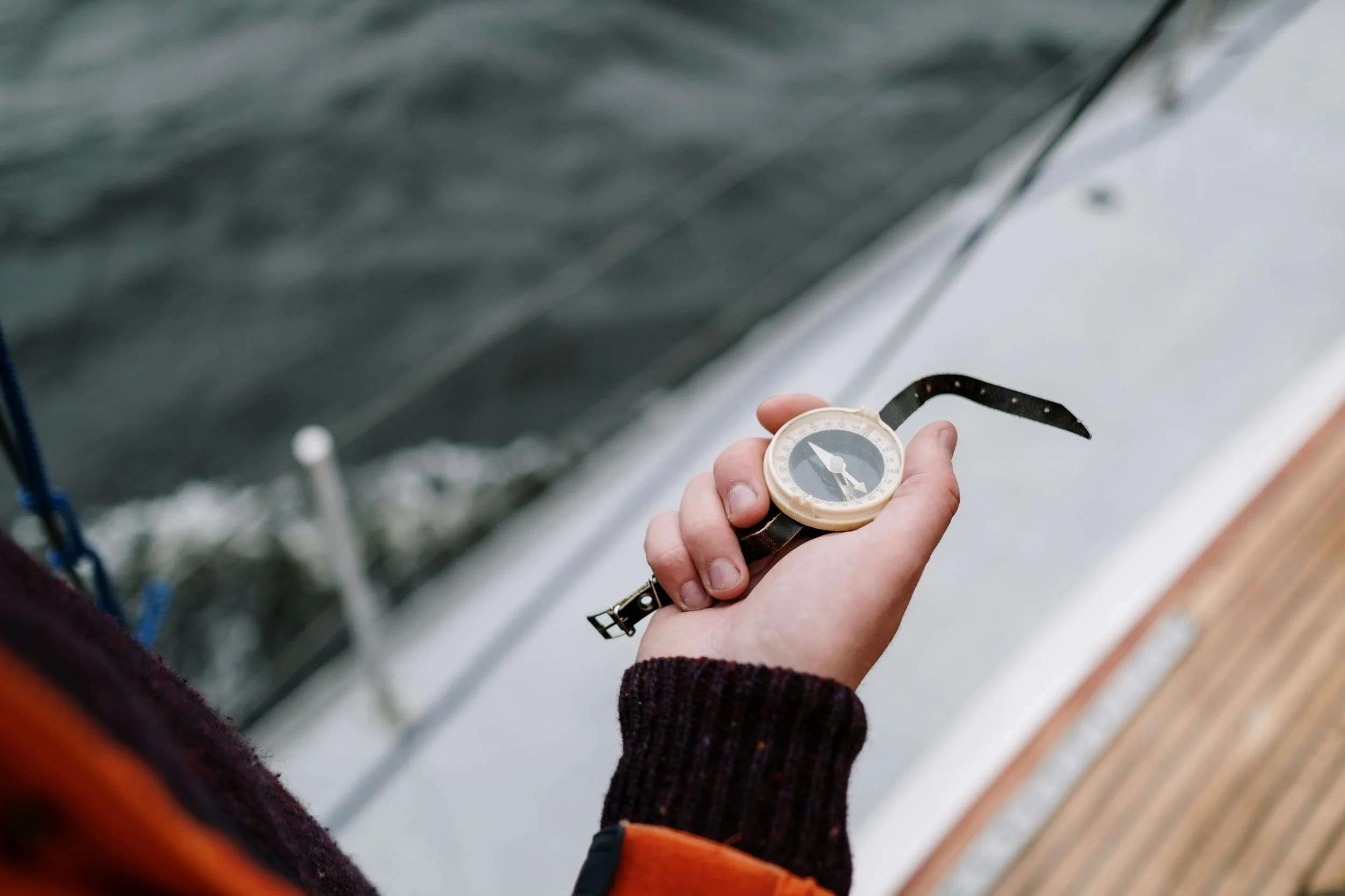 Close-up of a hand holding a compass on a boat, with water in the background.