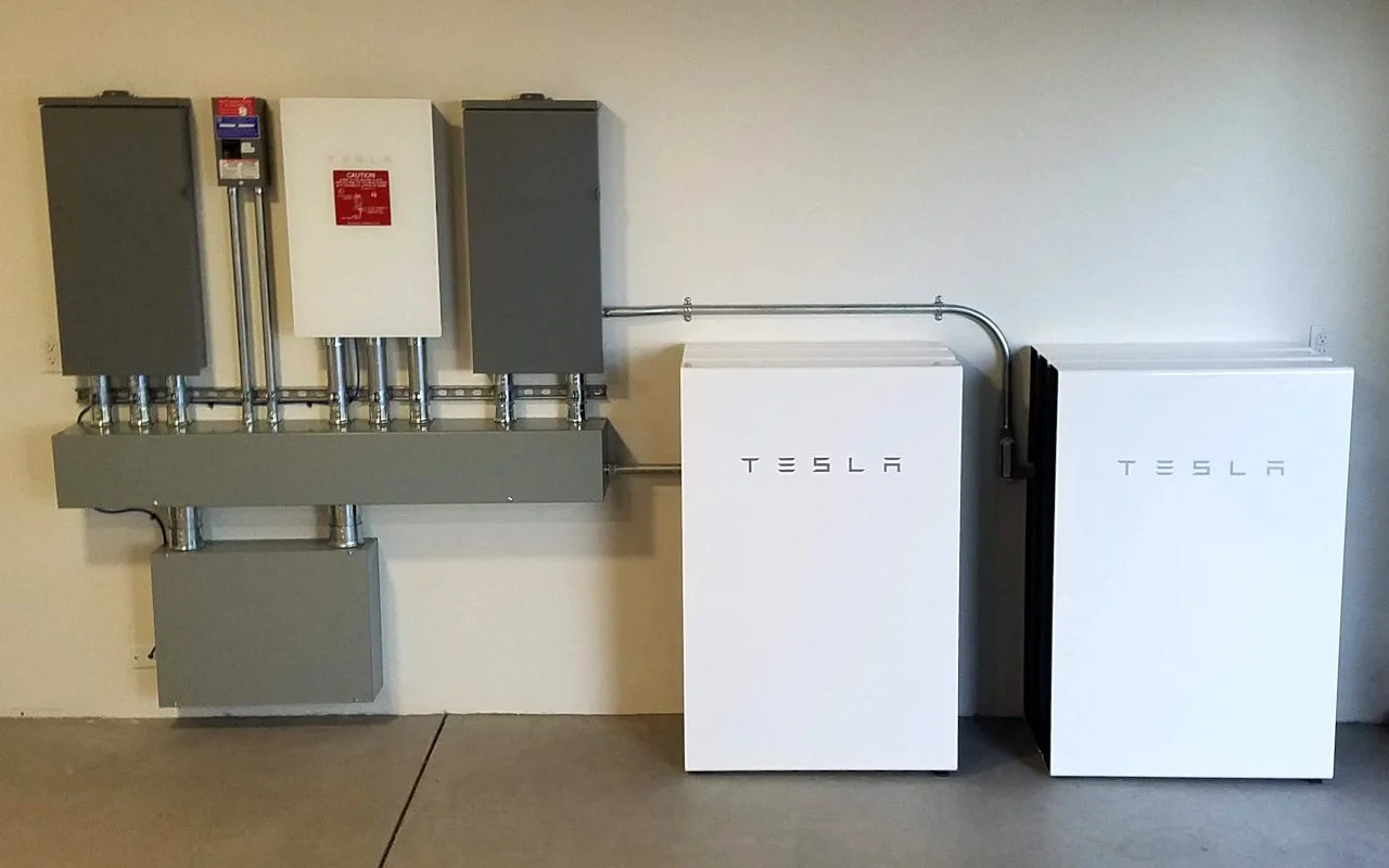 Electrical panels and Tesla Powerwalls installed on a beige wall.