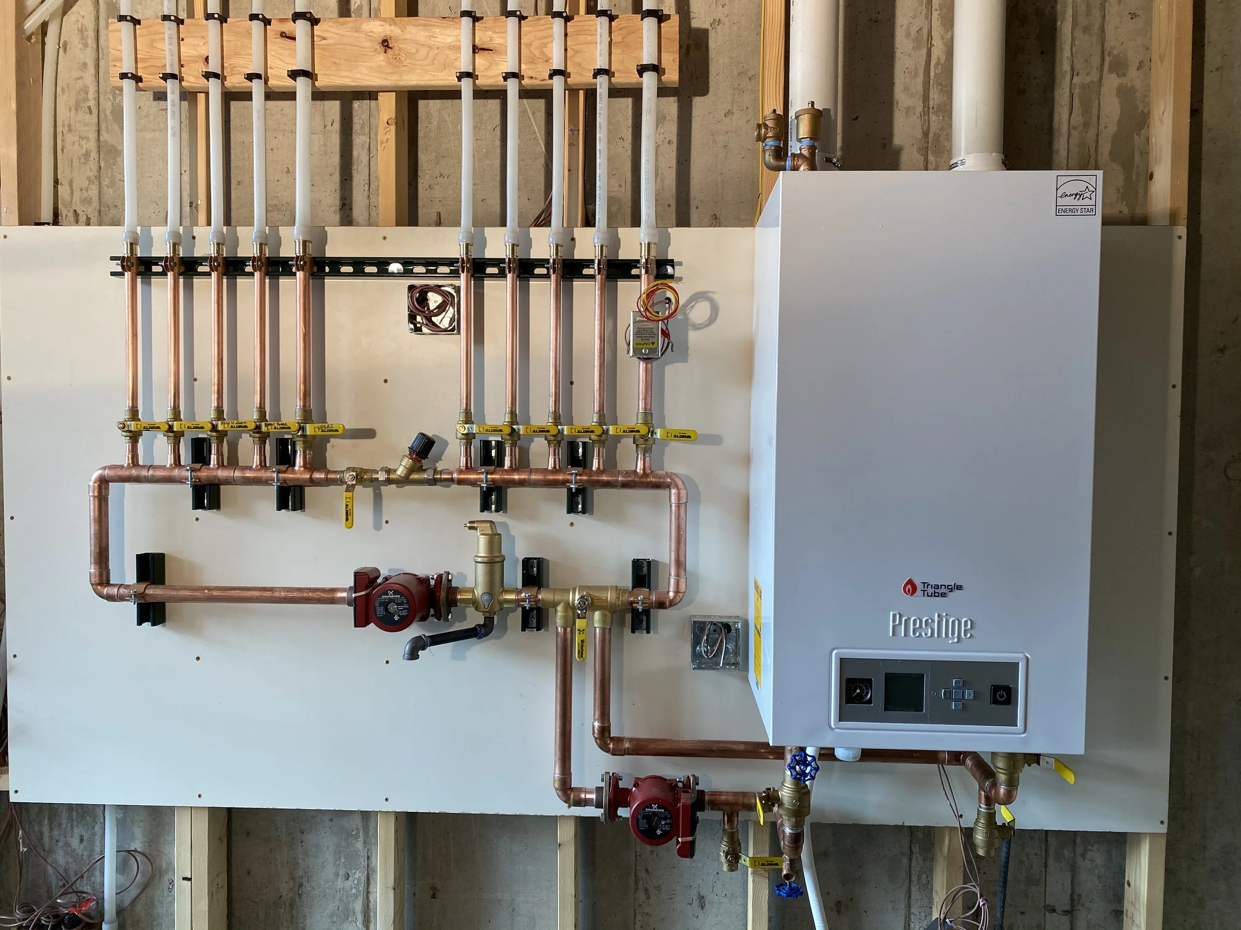 A plumbing system with copper pipes, valves, and a white boiler mounted on a wall. The boiler has a digital display and control panel.