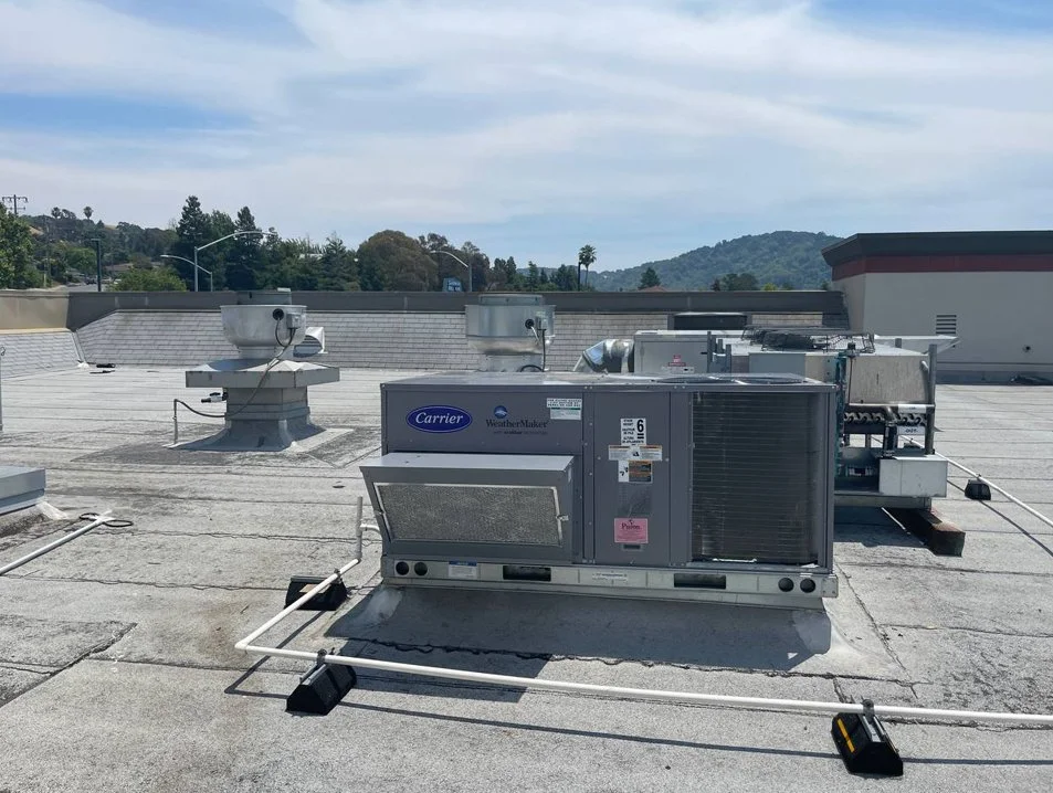 HVAC system on a building rooftop with a Carrier WeatherMaker unit and multiple vents, ducts, and electrical components visible.