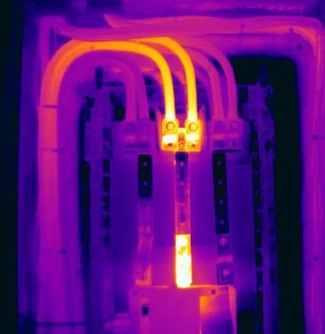 Thermal image of electrical wiring inside a panel with three cables connected to a switch or breaker.