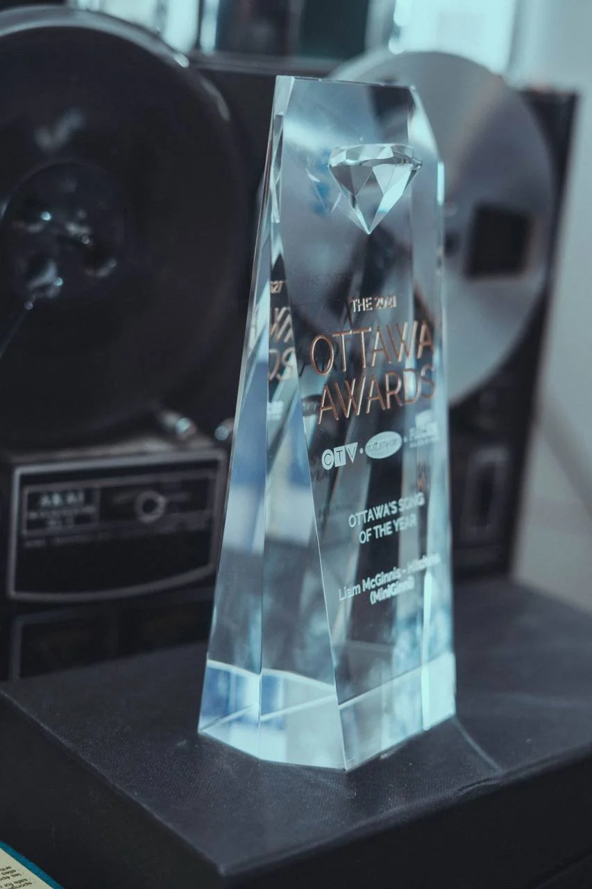 A crystal award trophy named 'Ottawa Awards' with a diamond engraving at the top, placed on a black surface. The award celebrates 'Ottawa’s Screen of the Year' and is awarded to Liam McClenahan in the category of 'Managing'.