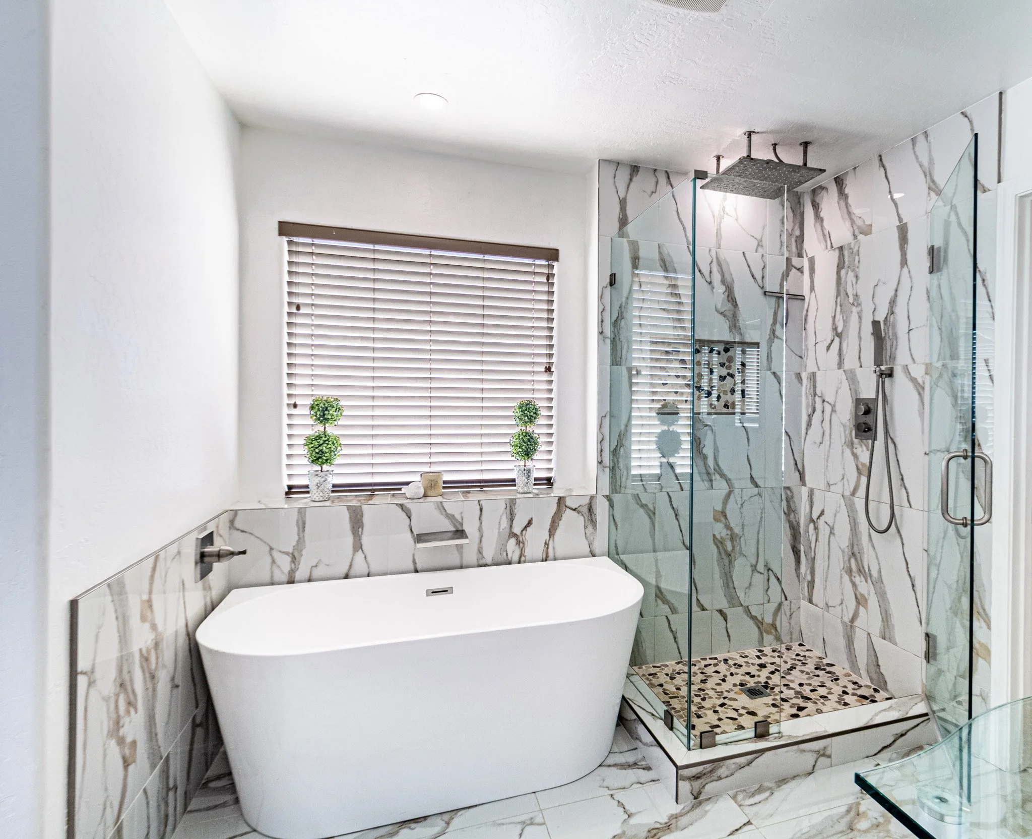 Modern bathroom with a freestanding bathtub, marble tile walls, and a glass-enclosed shower with a rainfall showerhead.