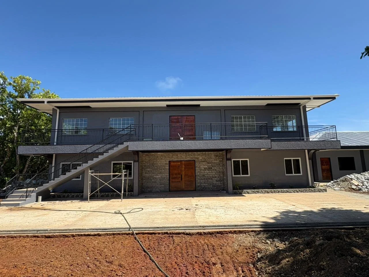 Two-story modern house with gray exterior, wooden front doors, large windows, and metal railing balcony, under a clear blue sky.
