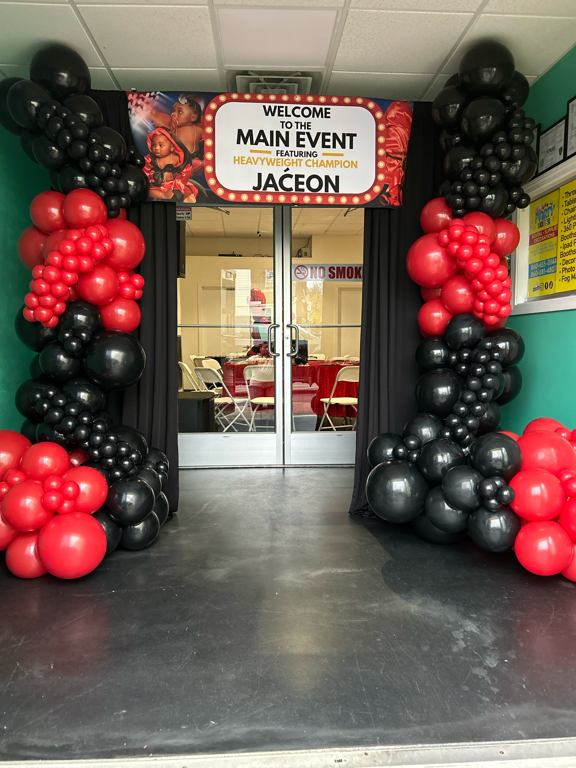 Entrance decorated with black and red balloons, with a banner above reading "Welcome to the Main Event featuring Heavyweight Champion Jaceon," showing images of a young girl boxing.