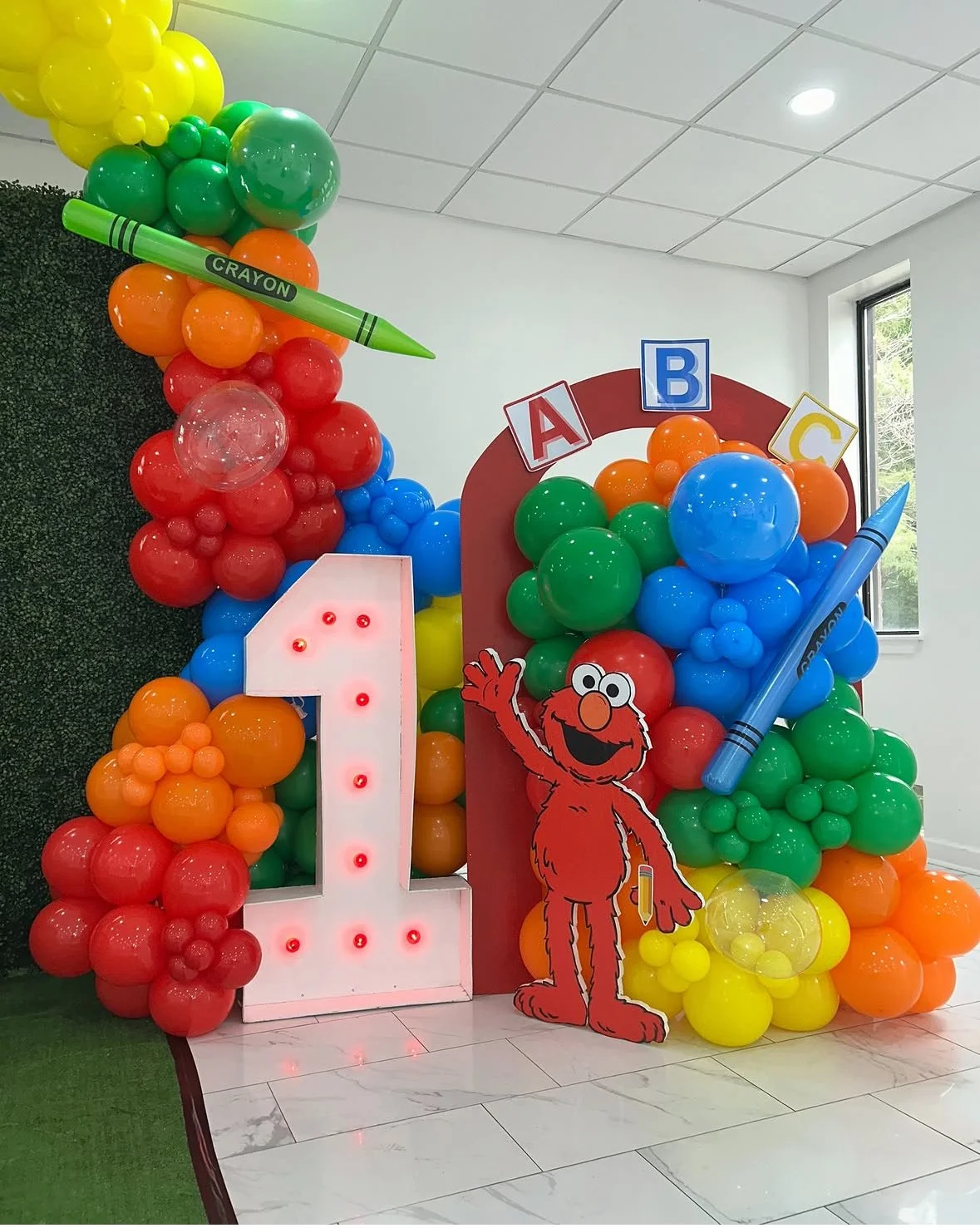Colorful balloon decoration with a number 1, Ernie character, large crayons, and alphabet blocks.