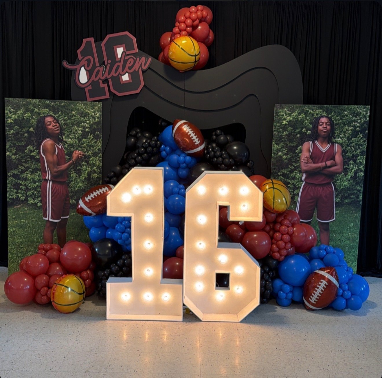 Decorative display celebrating Caiden's 13th birthday with sports theme featuring balloons in red, blue, black, and yellow, large illuminated number 13, and photographs of a young girl in a maroon sports uniform in front of green foliage.