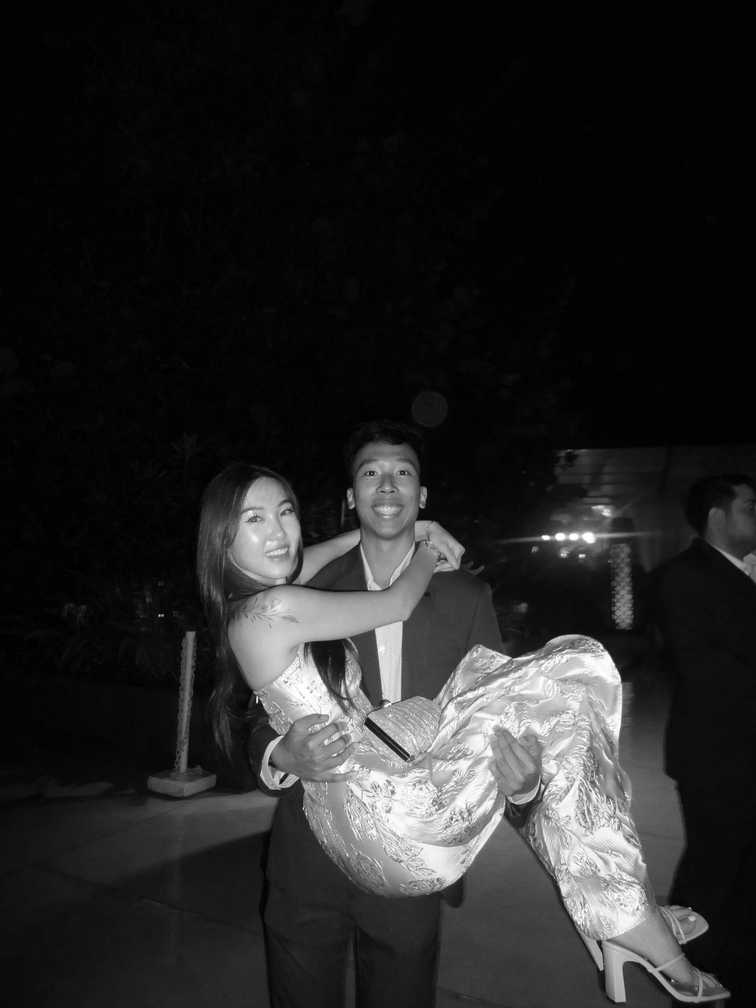 A young man in a suit holding a young woman in an elegant dress and high heels at night.