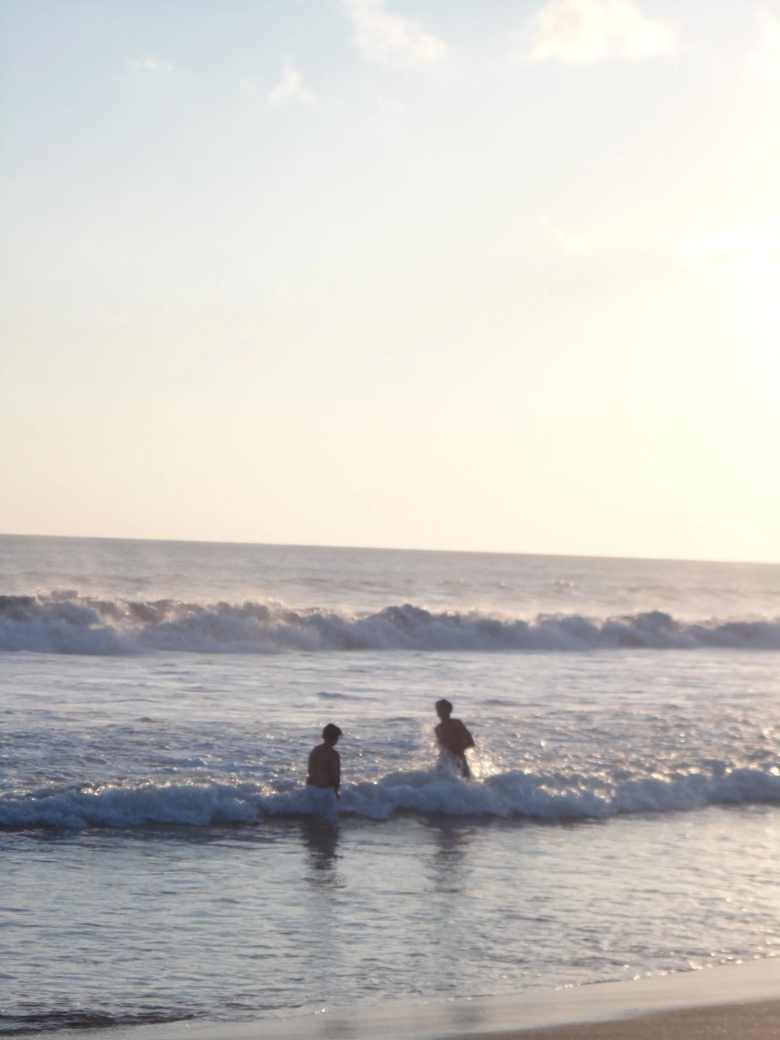 Two children playing in the ocean waves at sunset.