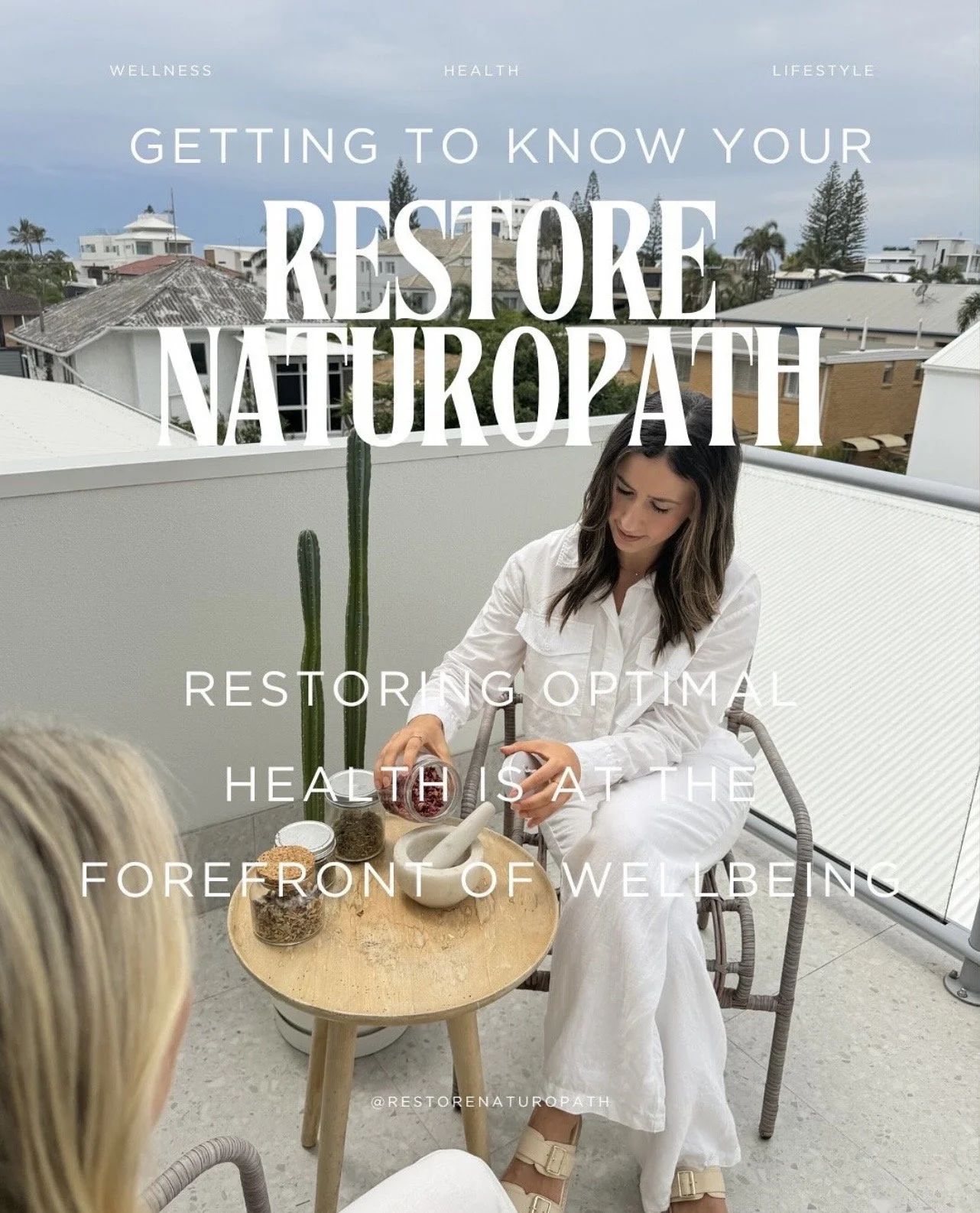 A woman in white clothing seated on a balcony, pouring herbs or spices into a mortar and pestle, with a small table holding jars and herbs, and a woman with blonde hair seated nearby.
