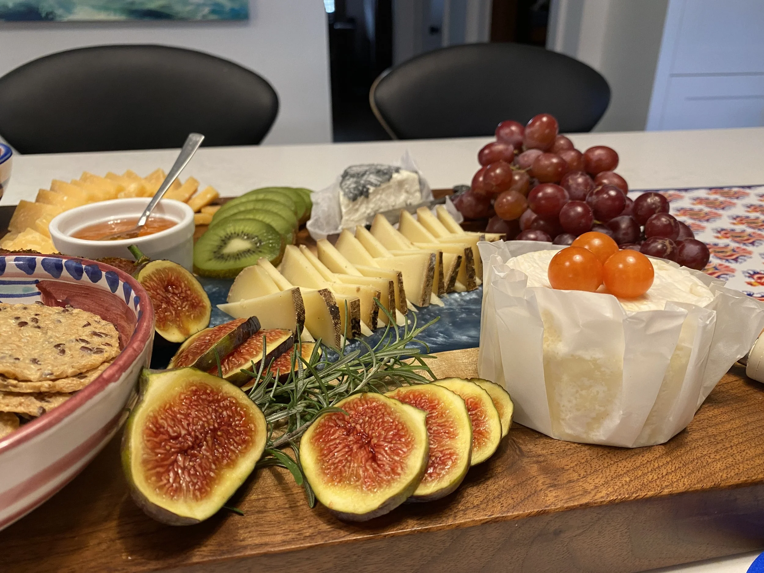 A cheese and fruit platter on a wooden board with grapes, figs, kiwi, and various cheeses