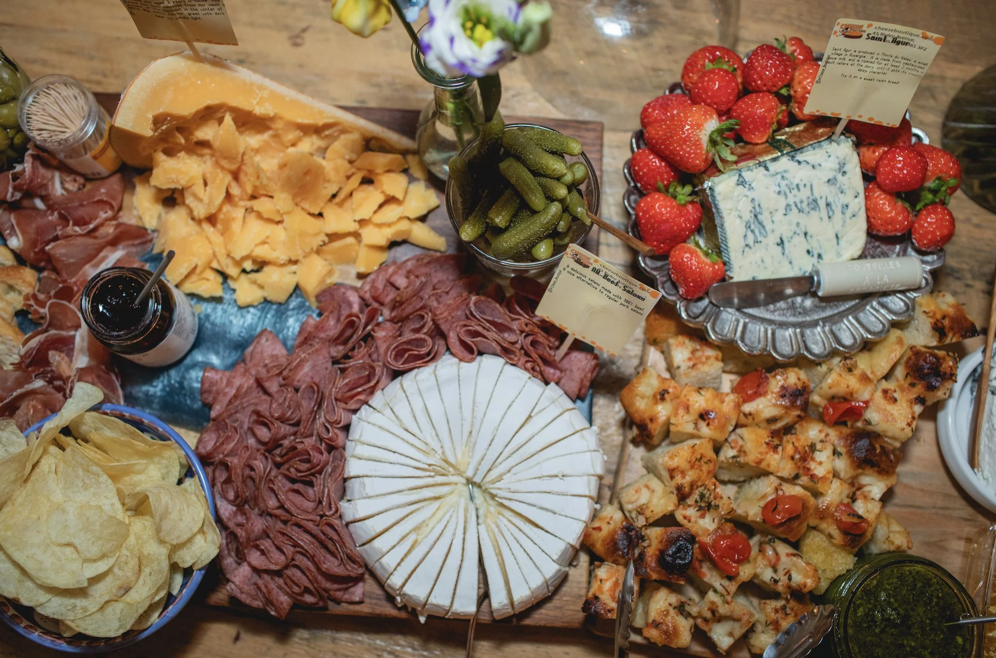 Close-up of a cheese and charcuterie board with strawberries, chips, pickles, cheeses, and cured meats.