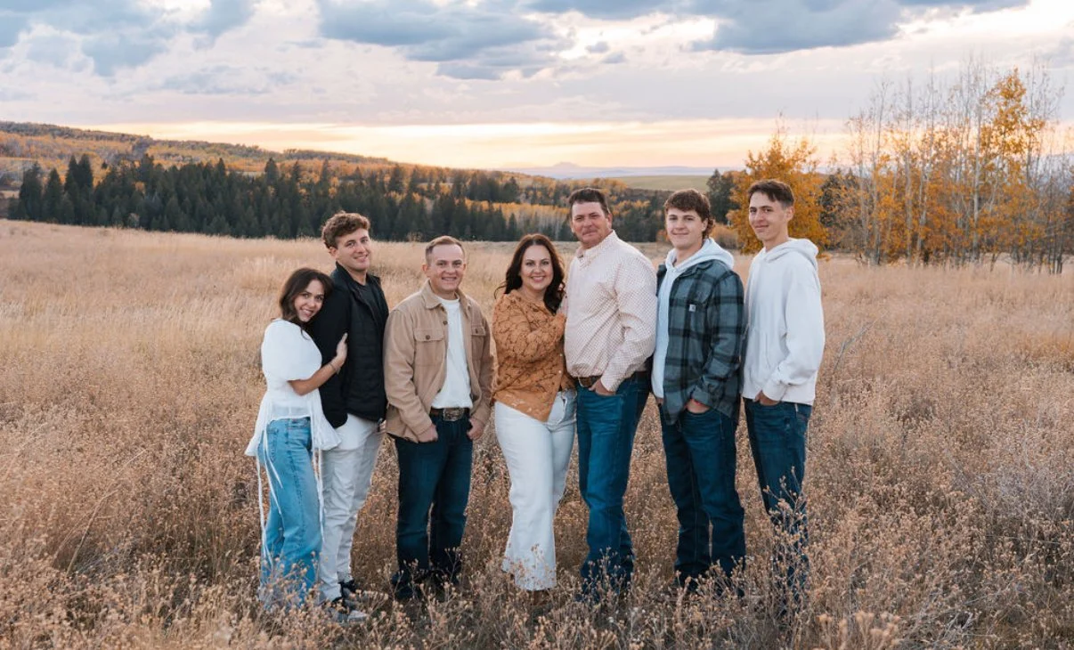 Family posing in a field during sunset with autumn trees in the background.