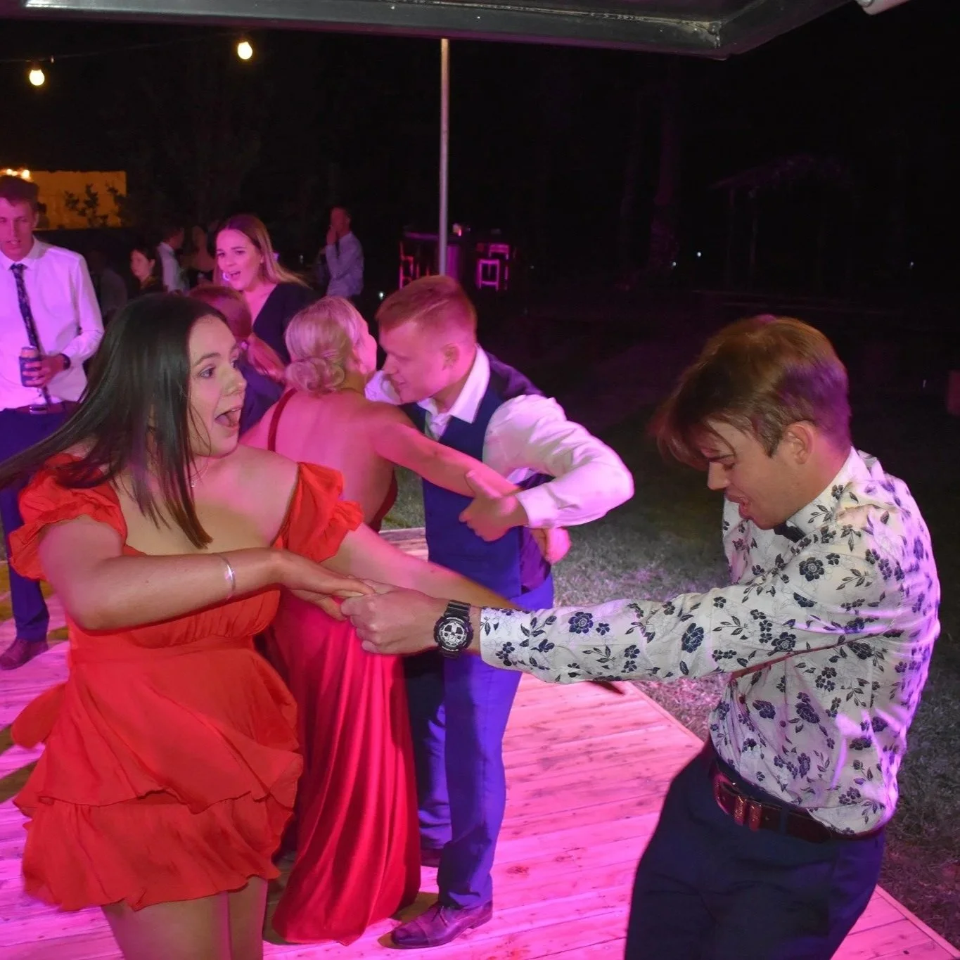 Young woman in red dress dancing happily at an outdoor party with groups of people dancing around her at night.