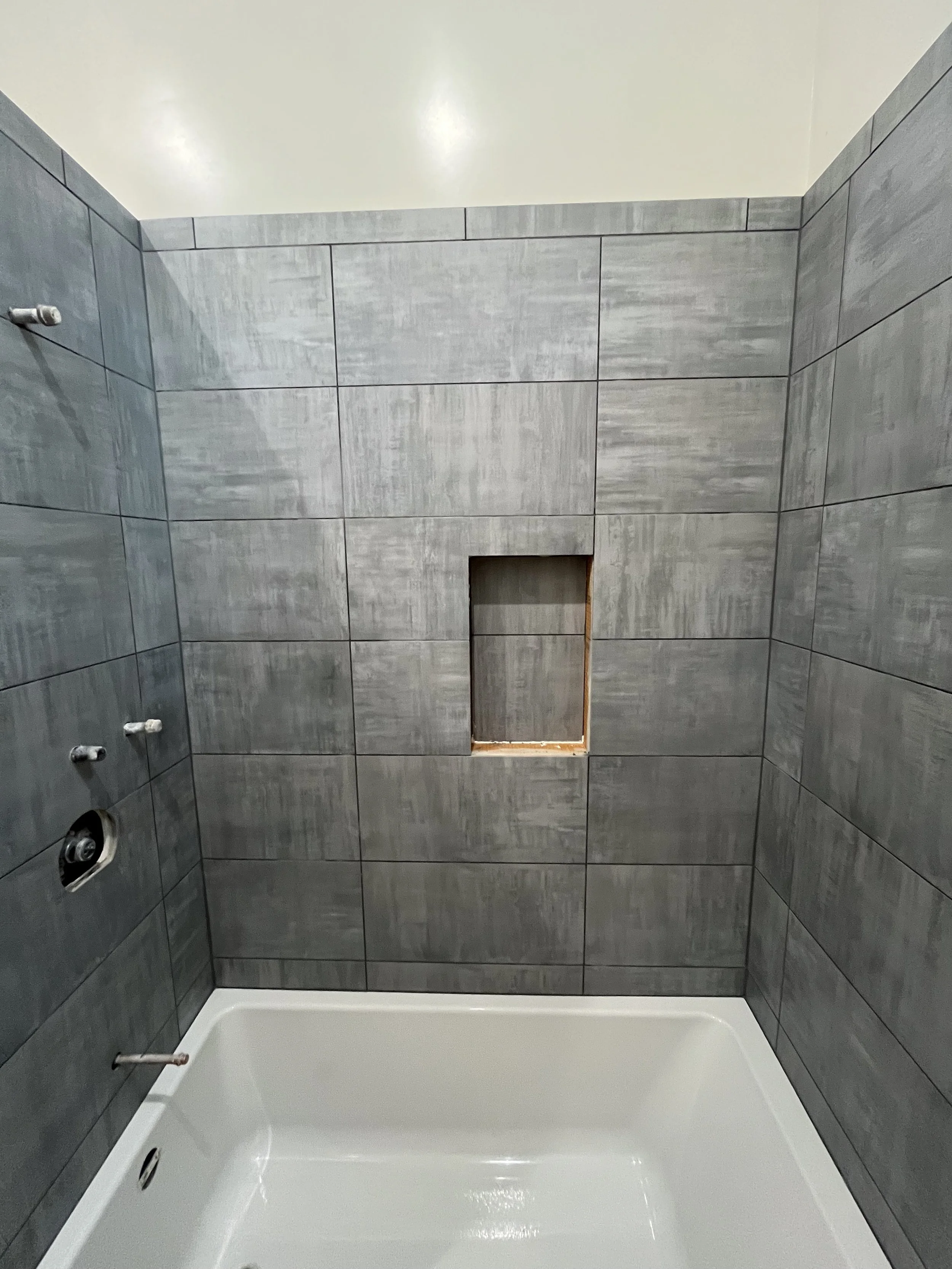 Modern bathroom shower renovation in Reno, NV featuring professional gray subway tile installation, a built-in storage niche, and a clean white bathtub surround.