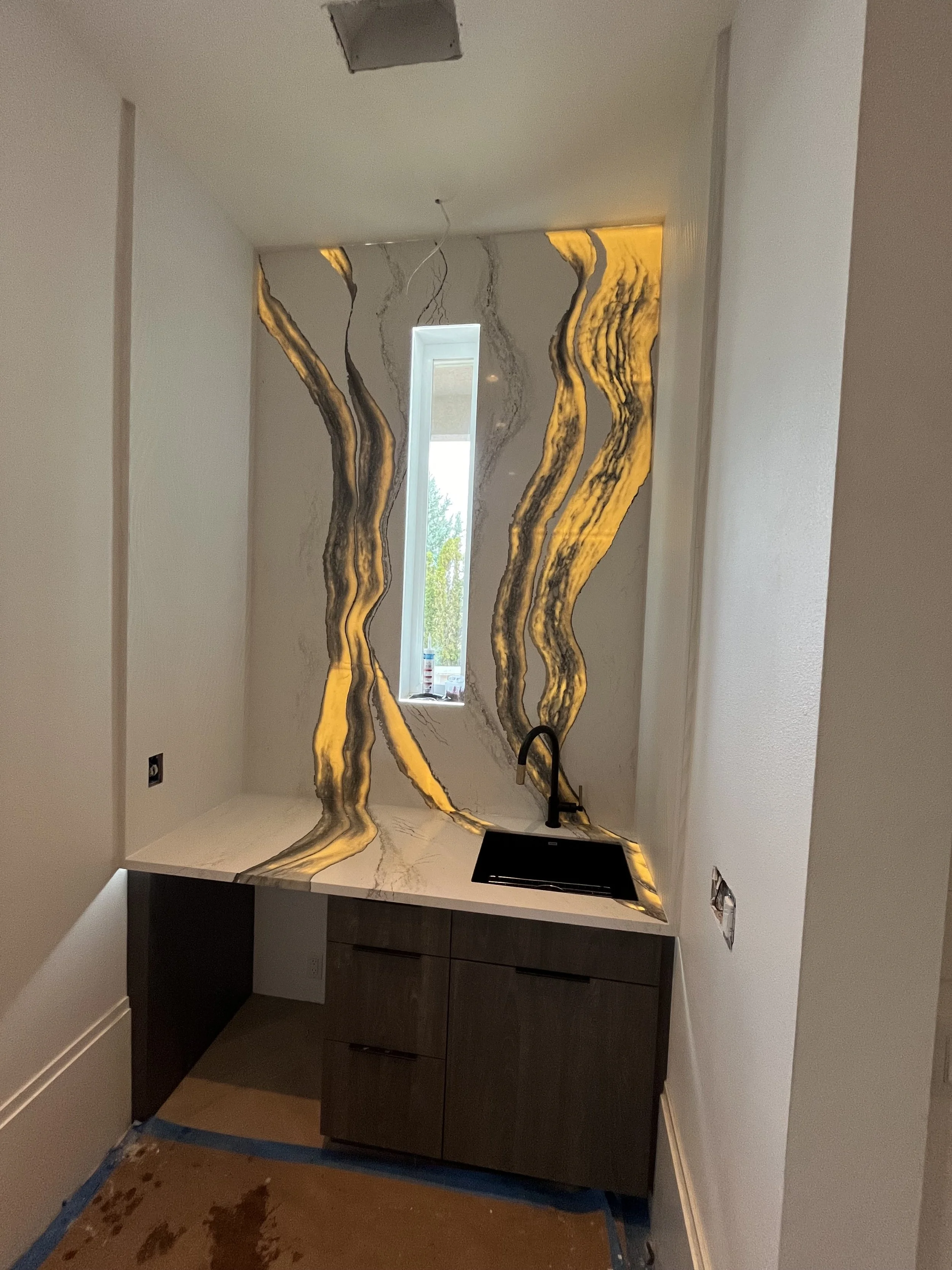 High-end basement game room vanity in Reno, NV featuring a backlit translucent stone backsplash wrapped with custom wavy tile accents.