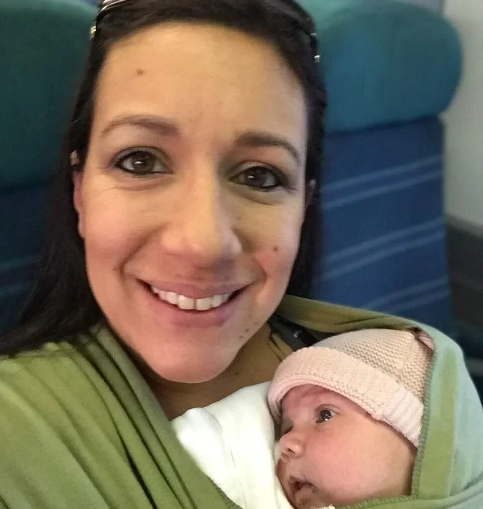 A woman holding a newborn baby wrapped in a green blanket, both smiling.
