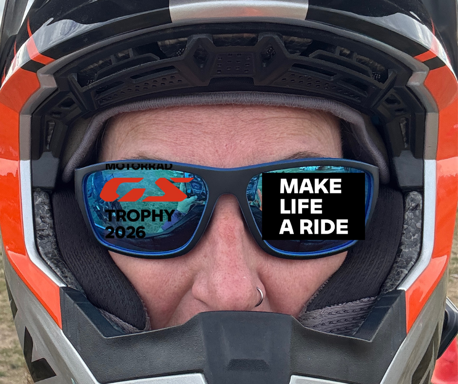 A person wearing a motorcycle helmet and sunglasses with a motivational message on the lenses, reading 'MAKE LIFE A RIDE' and 'GS TROPHY 2026'.