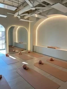 Interior of a modern yoga or meditation studio with mats, bolsters, and spherical meditation cushions, featuring soft lighting and arched wall designs.