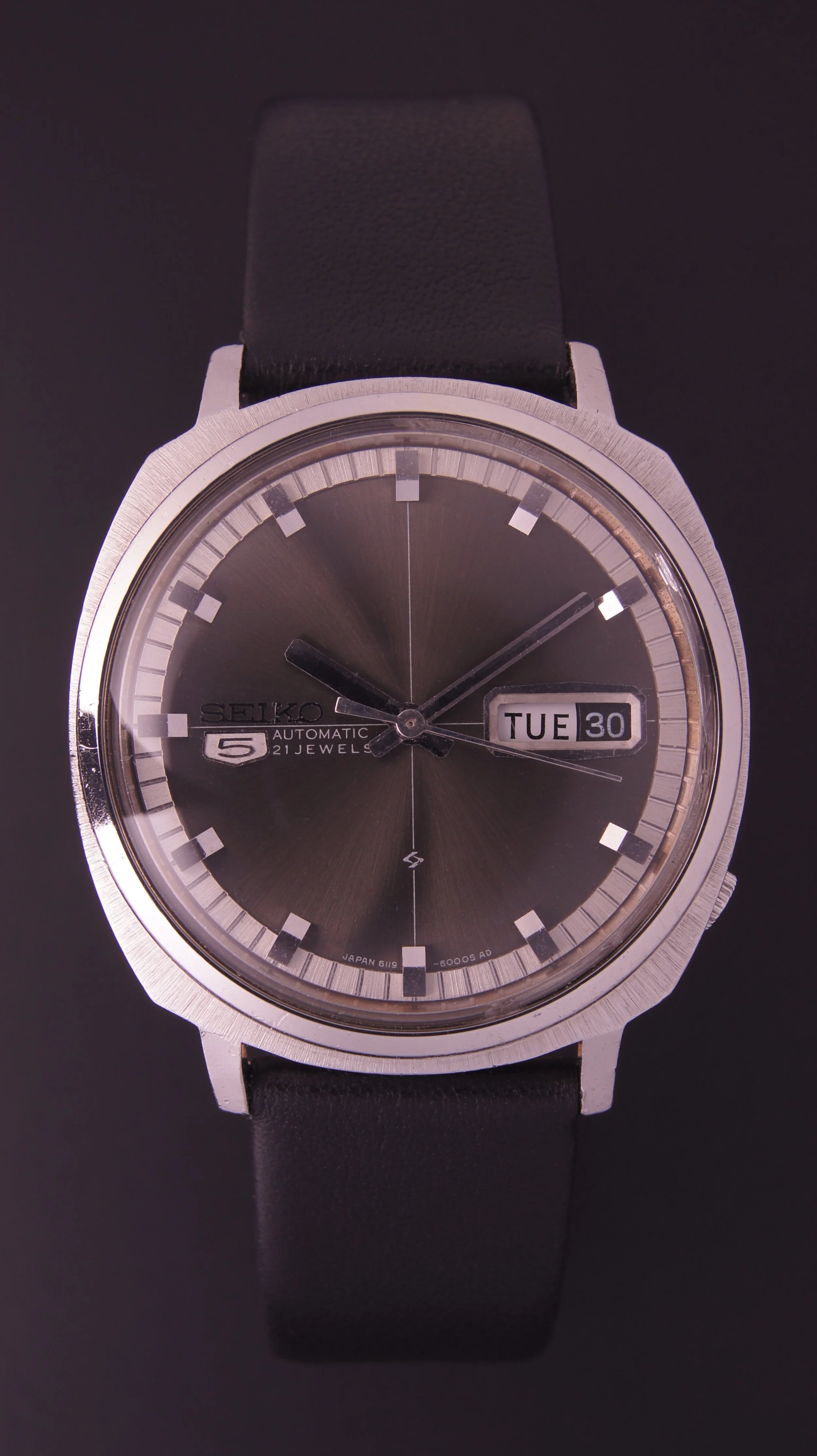 Seiko automatic wristwatch with black dial, silver case, black leather strap, displaying the time, day, and date.