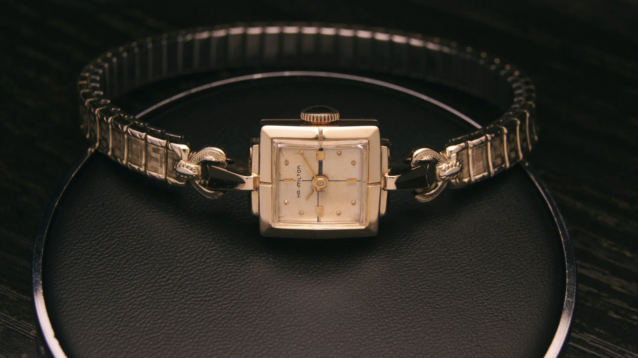 A vintage Hamilton wristwatch with a square silver face, gold markers, and a silver metal band.