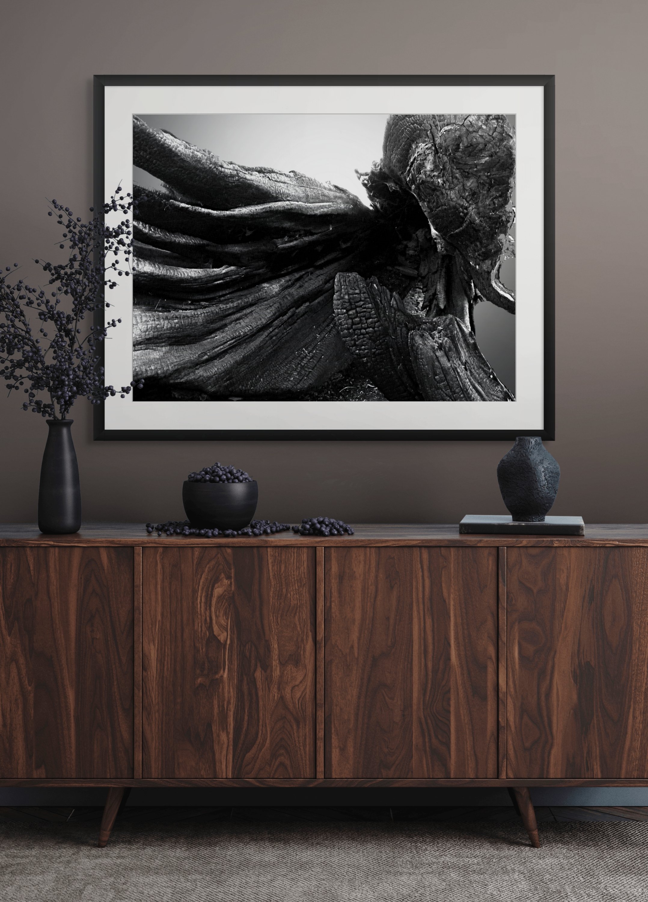 Decorative dresser with black vases, bowl with dark berries, and framed black and white abstract artwork on gray wall.