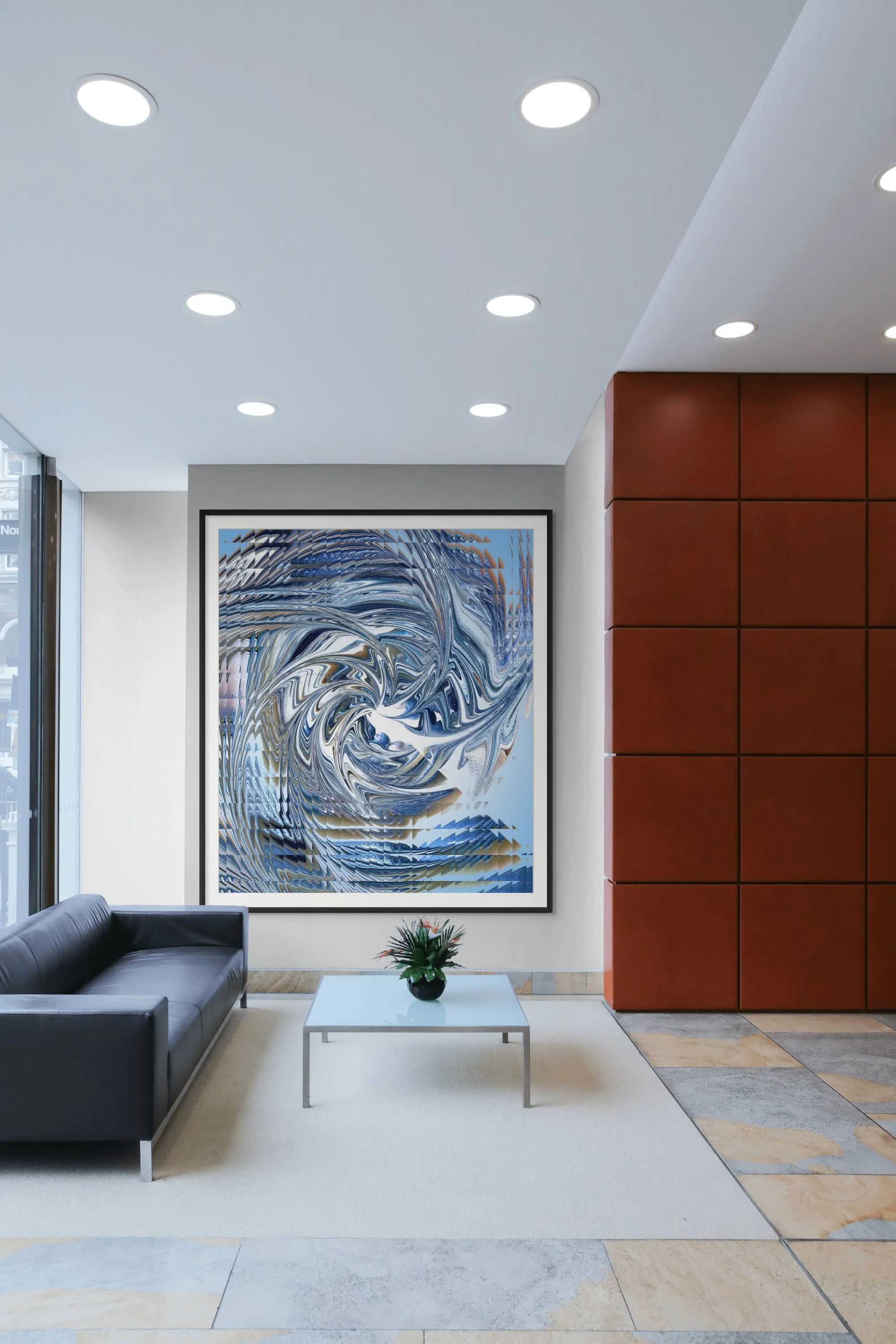 Modern hotel lobby with a framed abstract artwork, a black leather sofa, glass-top coffee table, and a plant in a black pot. White ceiling with recessed lighting, white and rust-colored wall accents, and large windows.