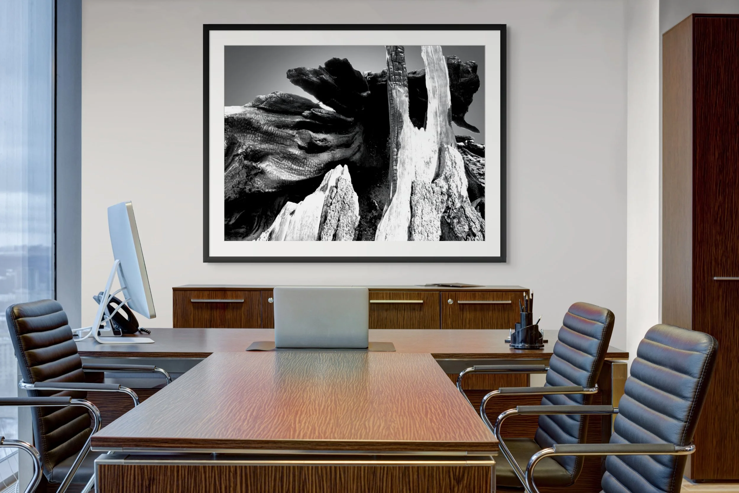 Black-and-white photograph of large rocks and driftwood stacked on a beach, framed and hung on a conference room wall.