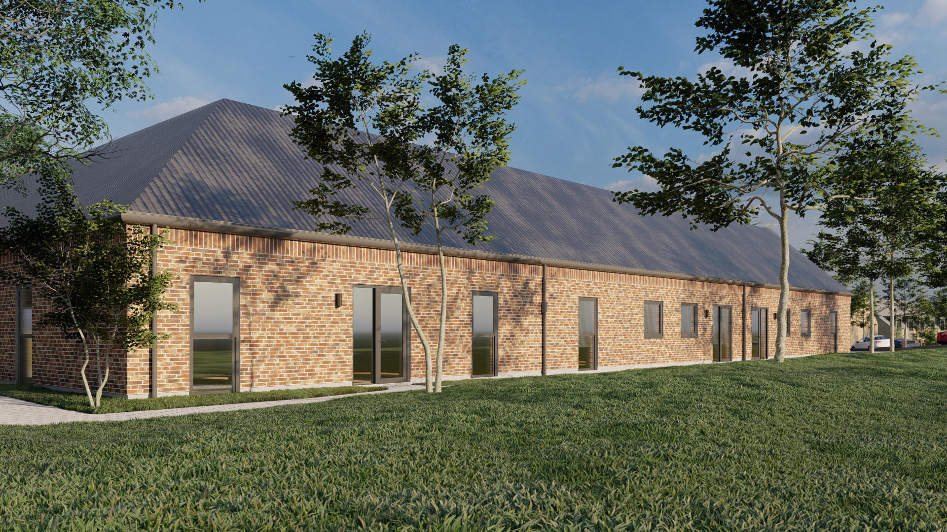 Lang, rødt murstensbygning med flere døre og vinduer, omgivet af grønne træer og græs, under en blå himmel.