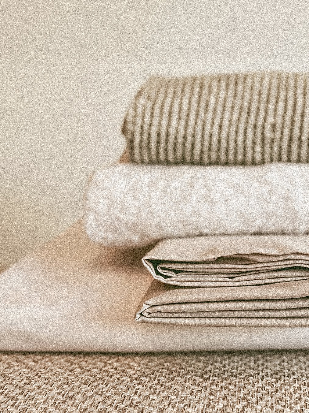 Stacked folded linens including towels, cloths, and fabric on a textured surface.