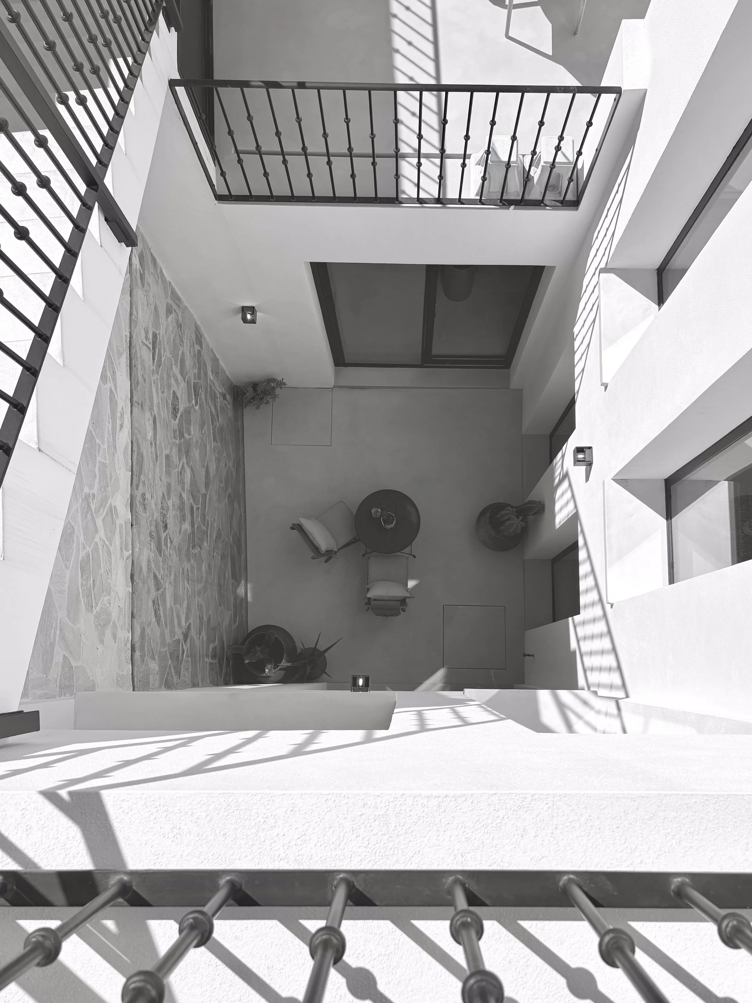 View from a balcony looking down into an outdoor patio area with a small round table, chairs, potted plants, and a stone floor.
