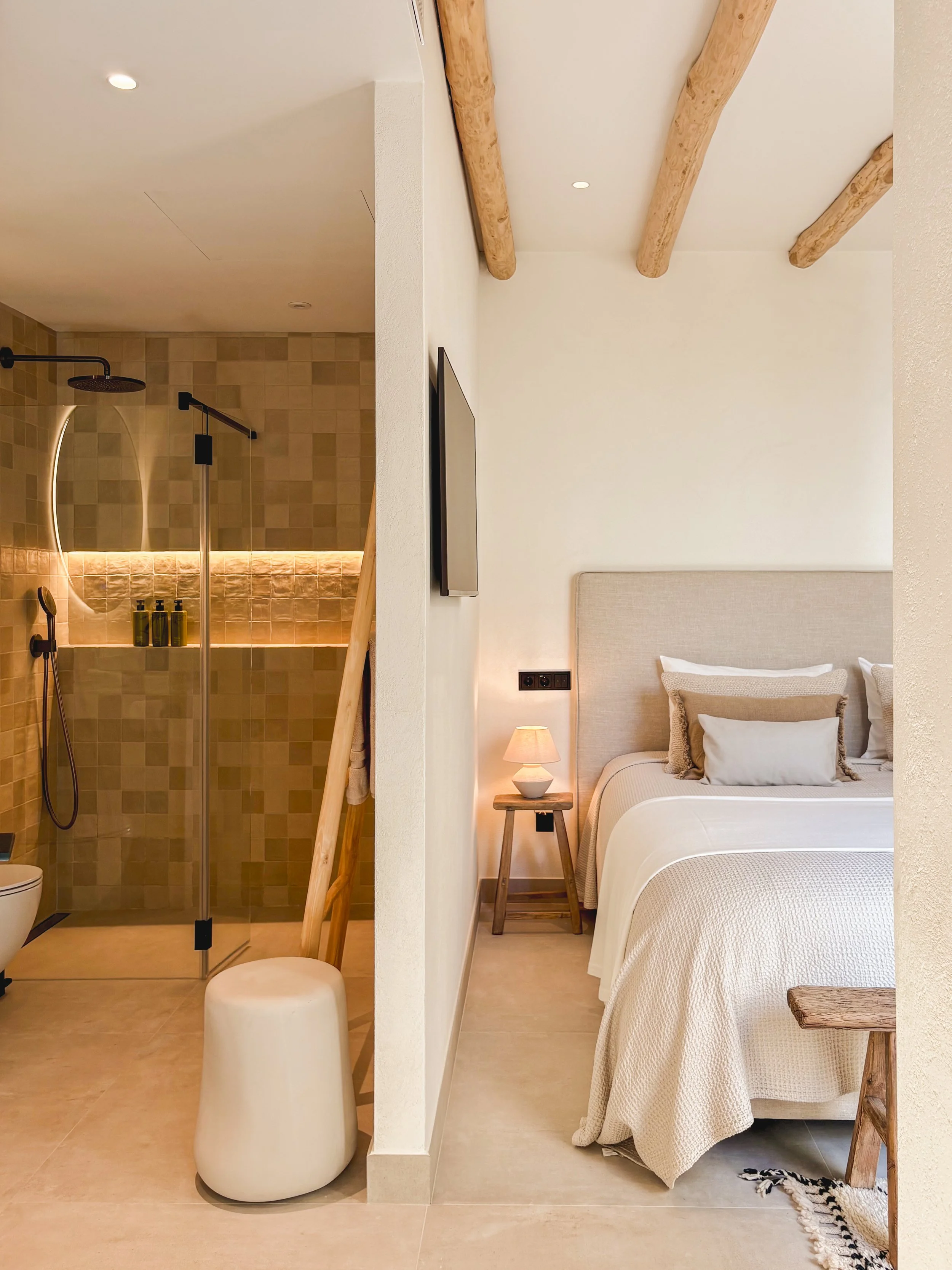 A cozy bedroom with a bed, nightstand, and lamp, separated from a modern walk-in shower by a wall, in a stylish interior design.