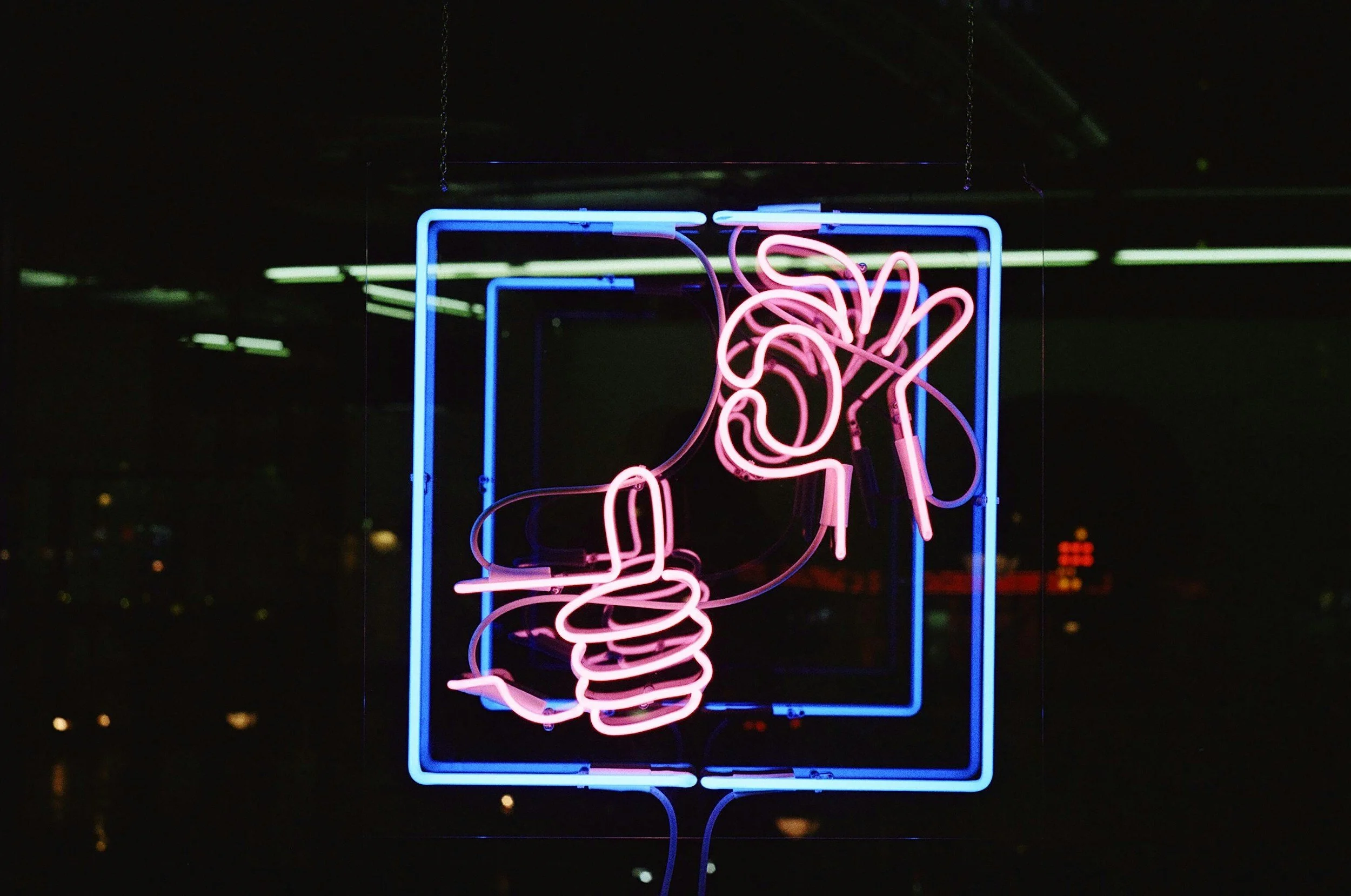 Neon sign of a hand holding a cigarette inside a blue square frame at night.