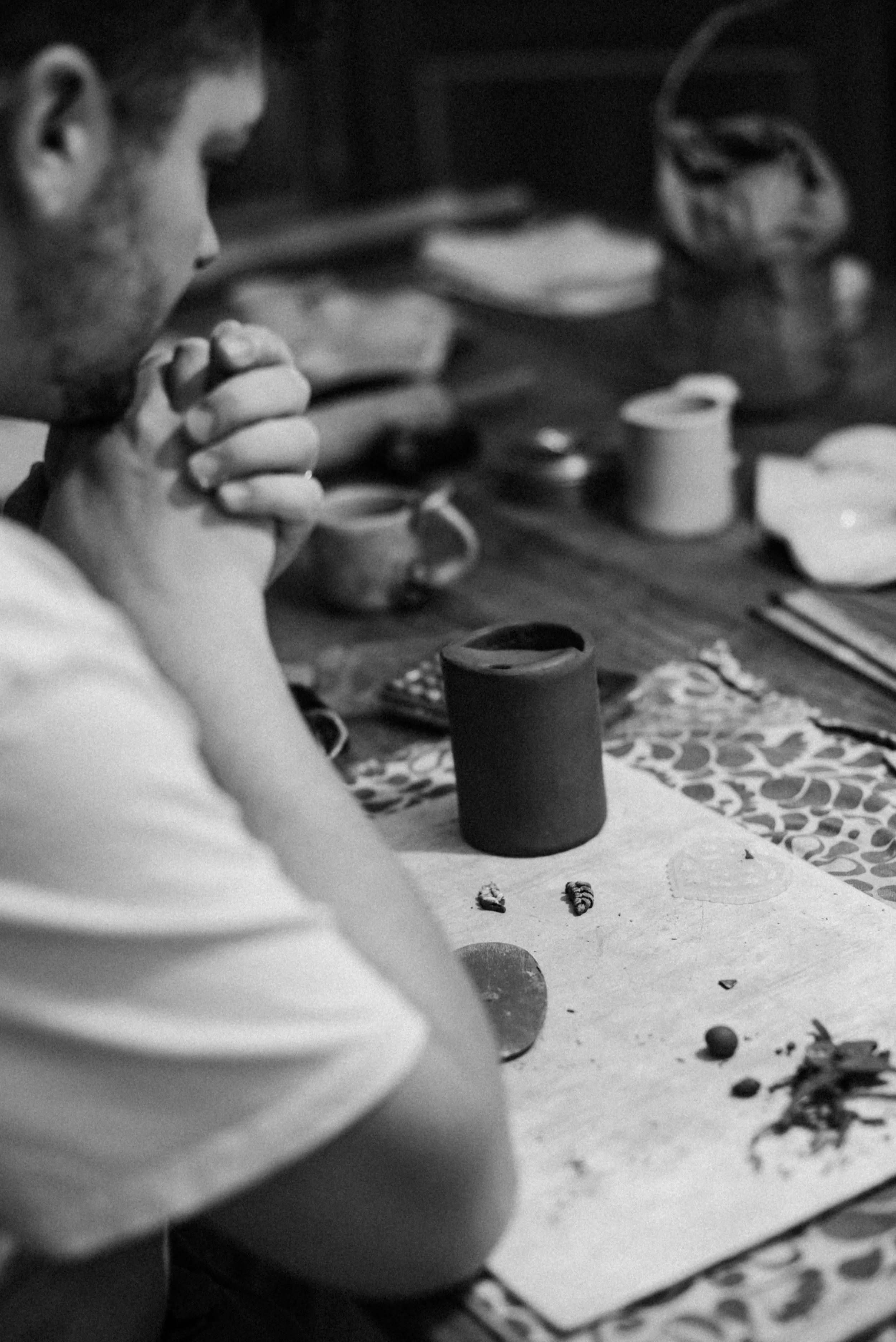 A person with pruney hands, sitting at a table with food and utensils, appears to be praying or in a moment of reflection.