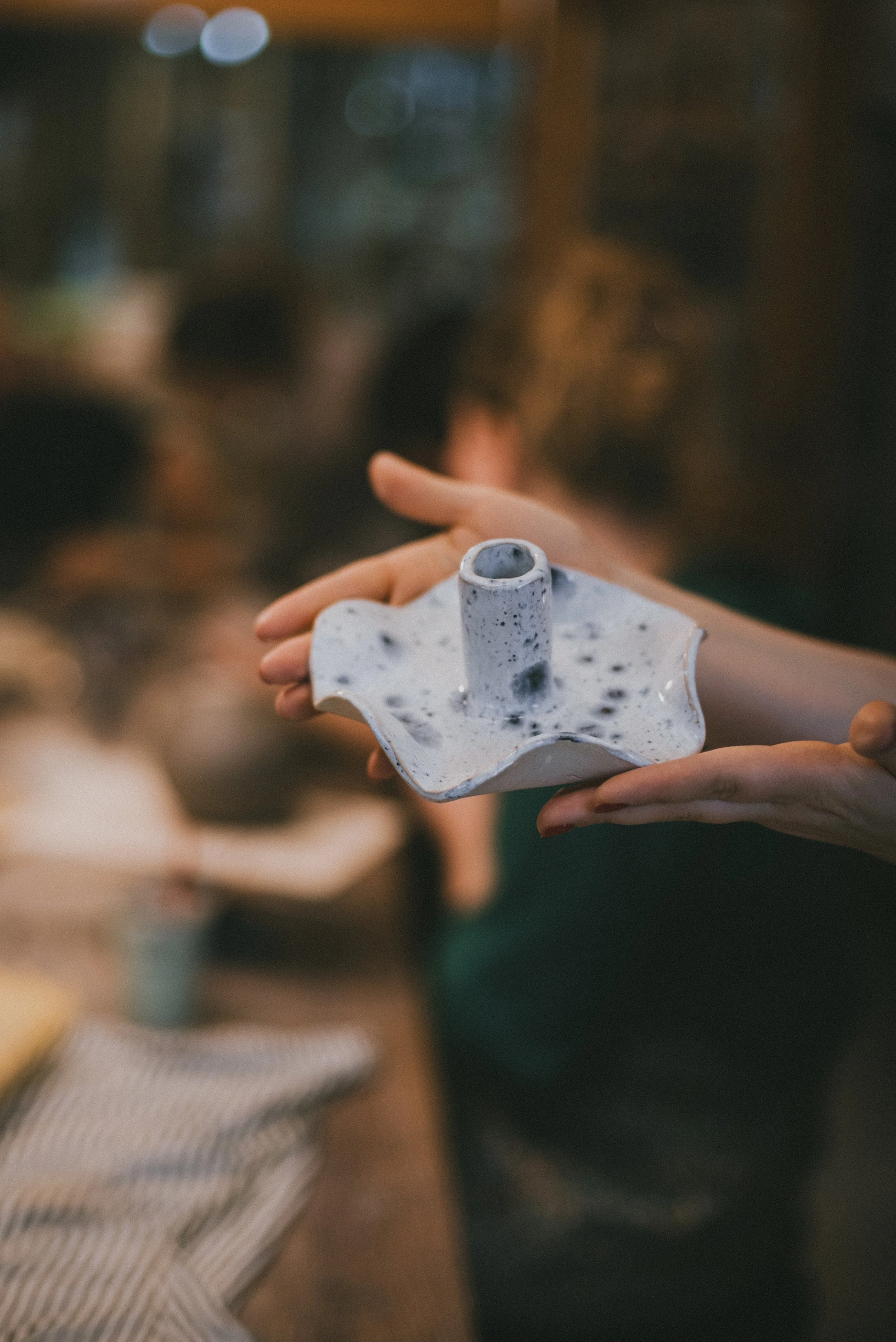 A person holding a white ceramic candle holder with black speckles, shaped like a flower with a central hollow