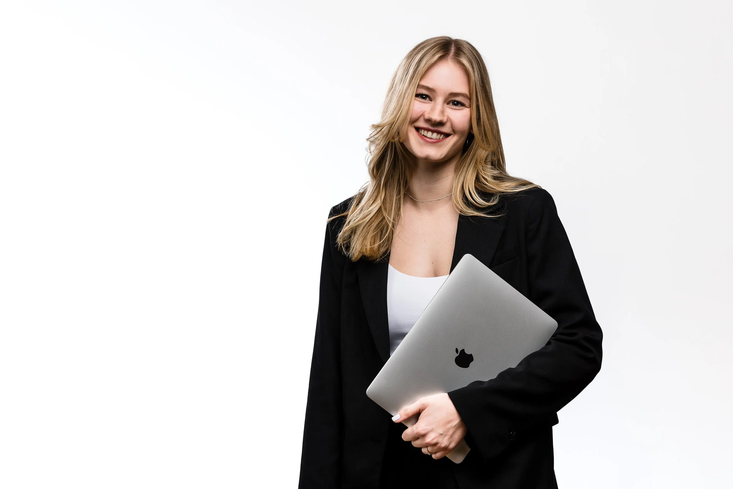 Junge Frau in Businesskleidung hält einen MacBook-Laptop vor einem weißen Hintergrund.