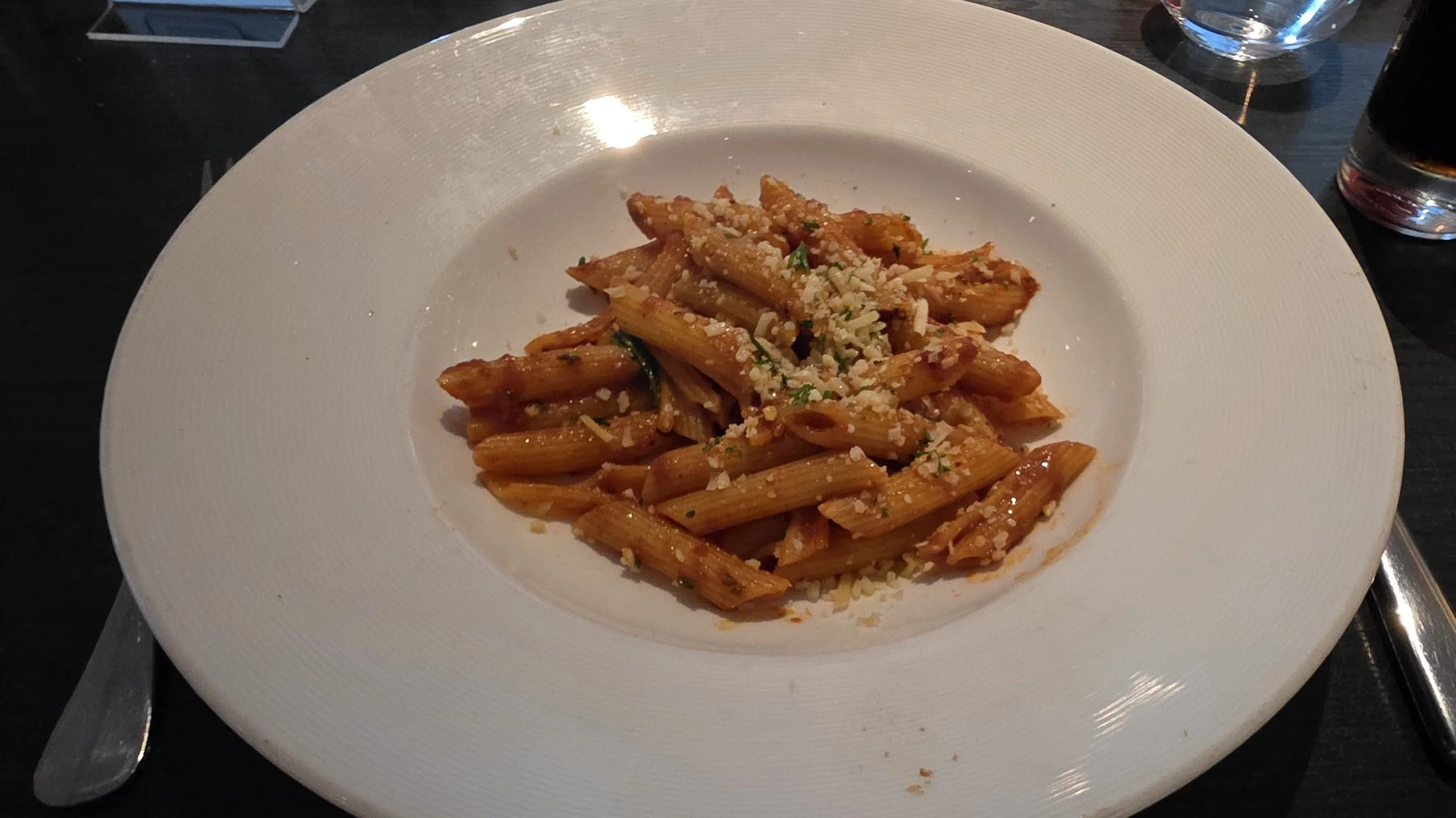 A plate of penne pasta with red sauce topped with grated cheese and herbs.