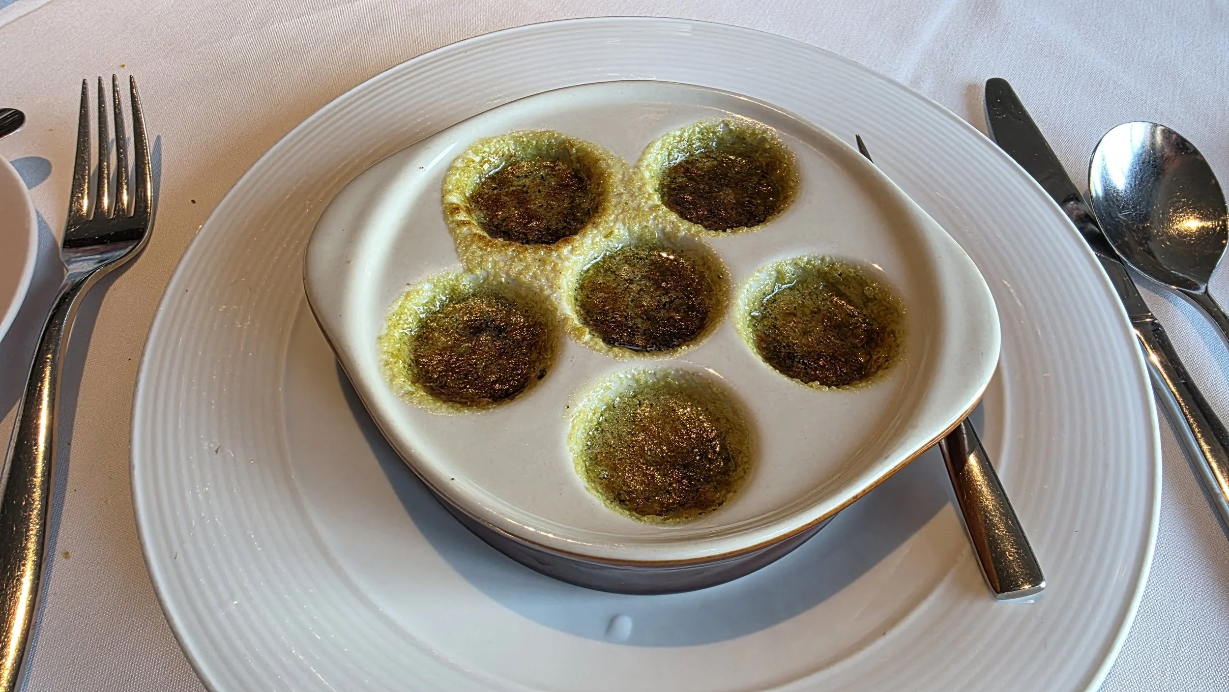 Baked eggs with green pesto in a white ramekin on a white plate, set on a table with utensils.