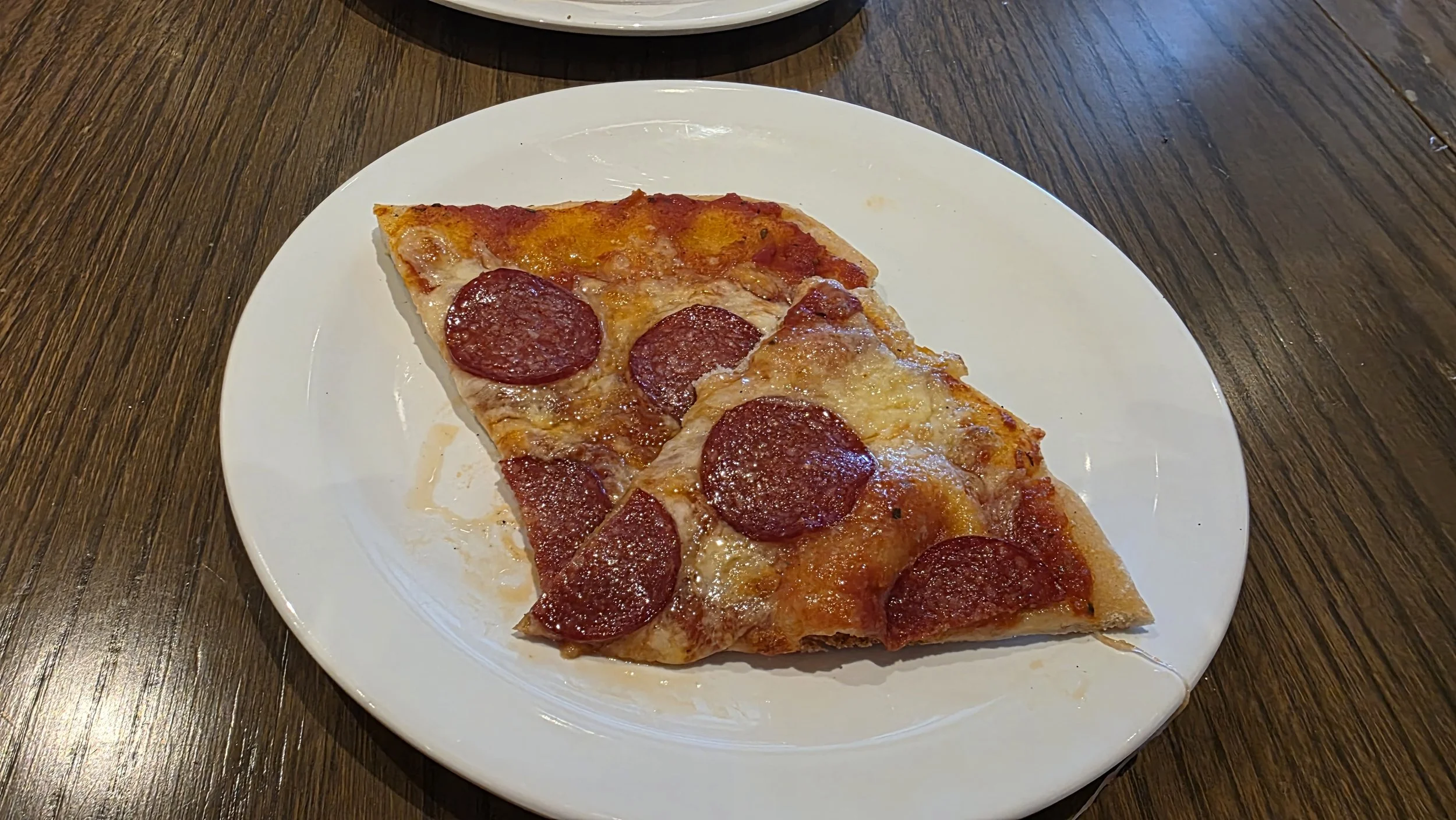 A slices pepperoni pizza on a white plate on a wooden table.