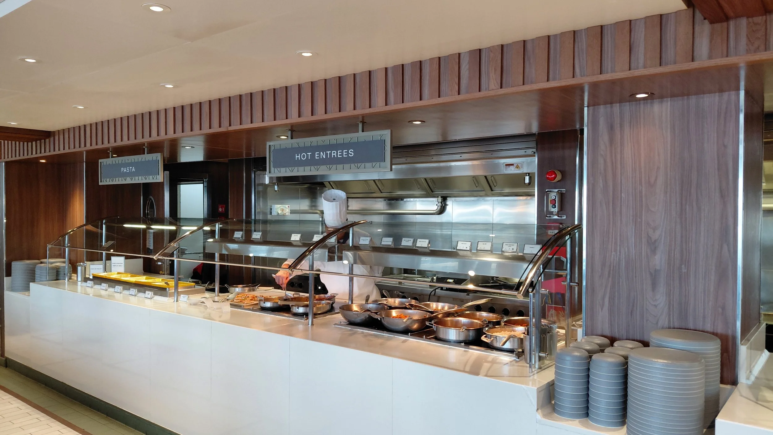 Buffet station with chafing dishes and utensils labeled for hot entrees, with a sign above labeled "HOT ENTREES."
