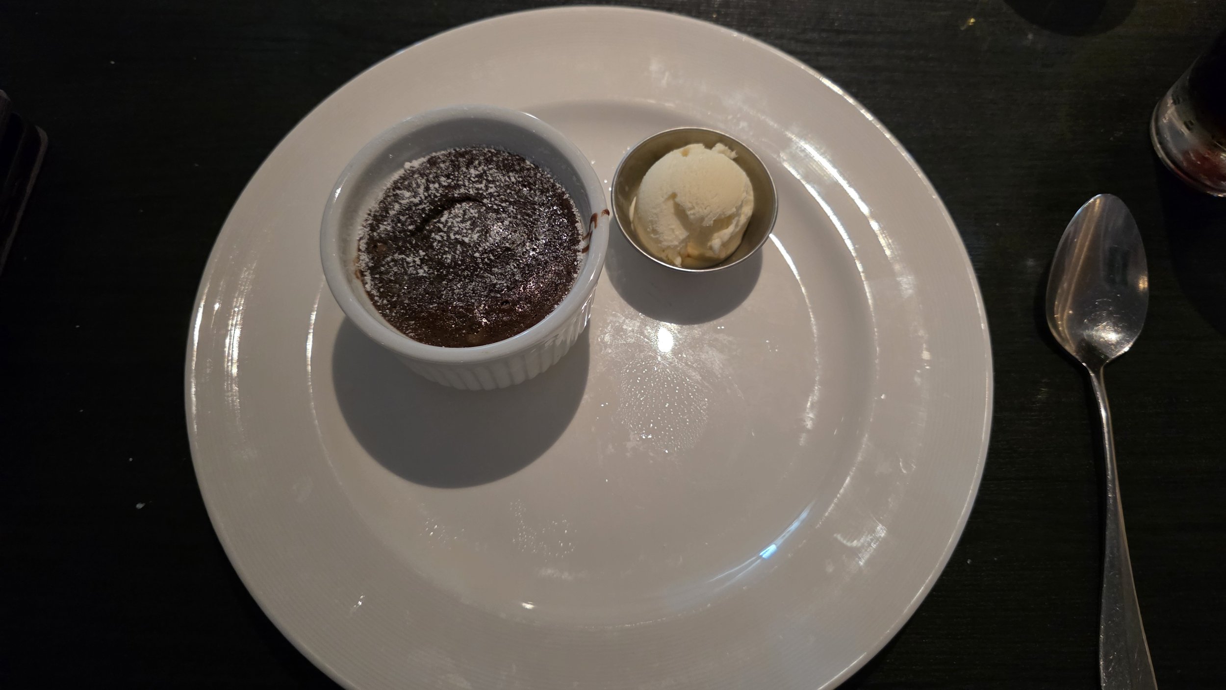 Chocolate lava cake with powdered sugar, a scoop of vanilla ice cream, and a spoon on a white plate.