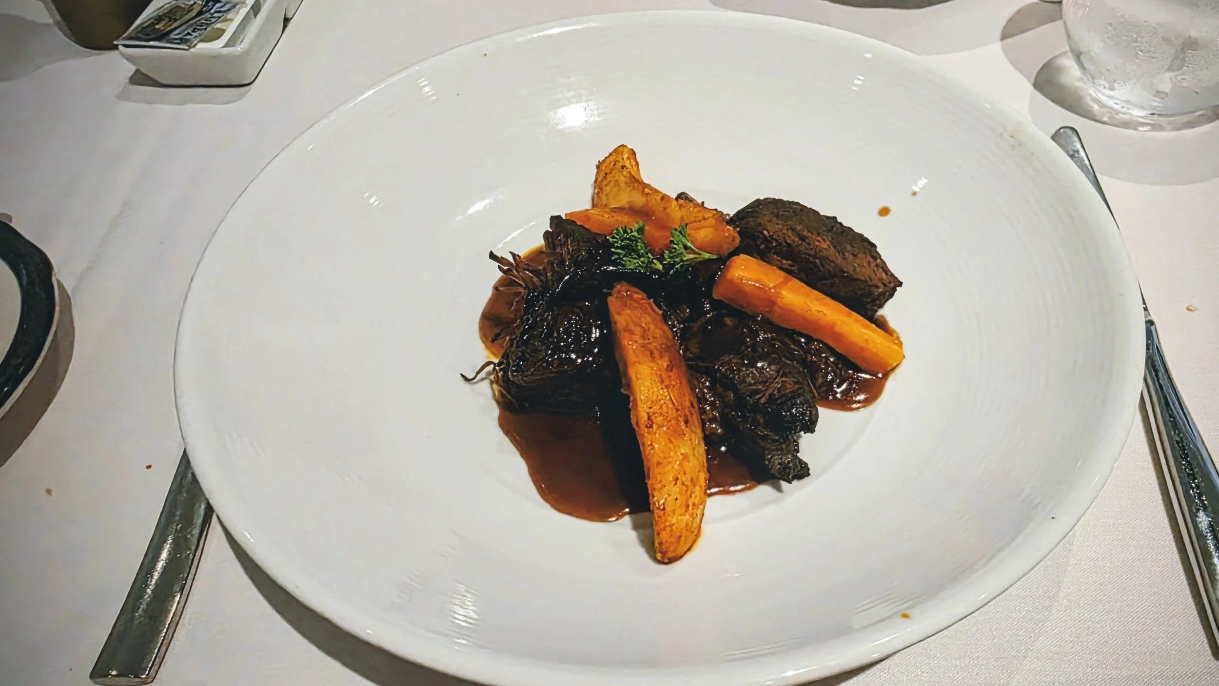 Plate of braised beef with carrots, garnished with parsley, served in a rich sauce