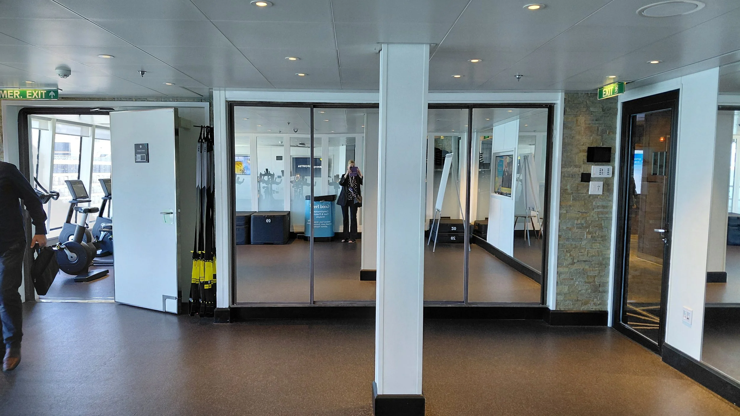 Interior of a gym or fitness center with exercise equipment, mirrors, and a person taking a photo.
