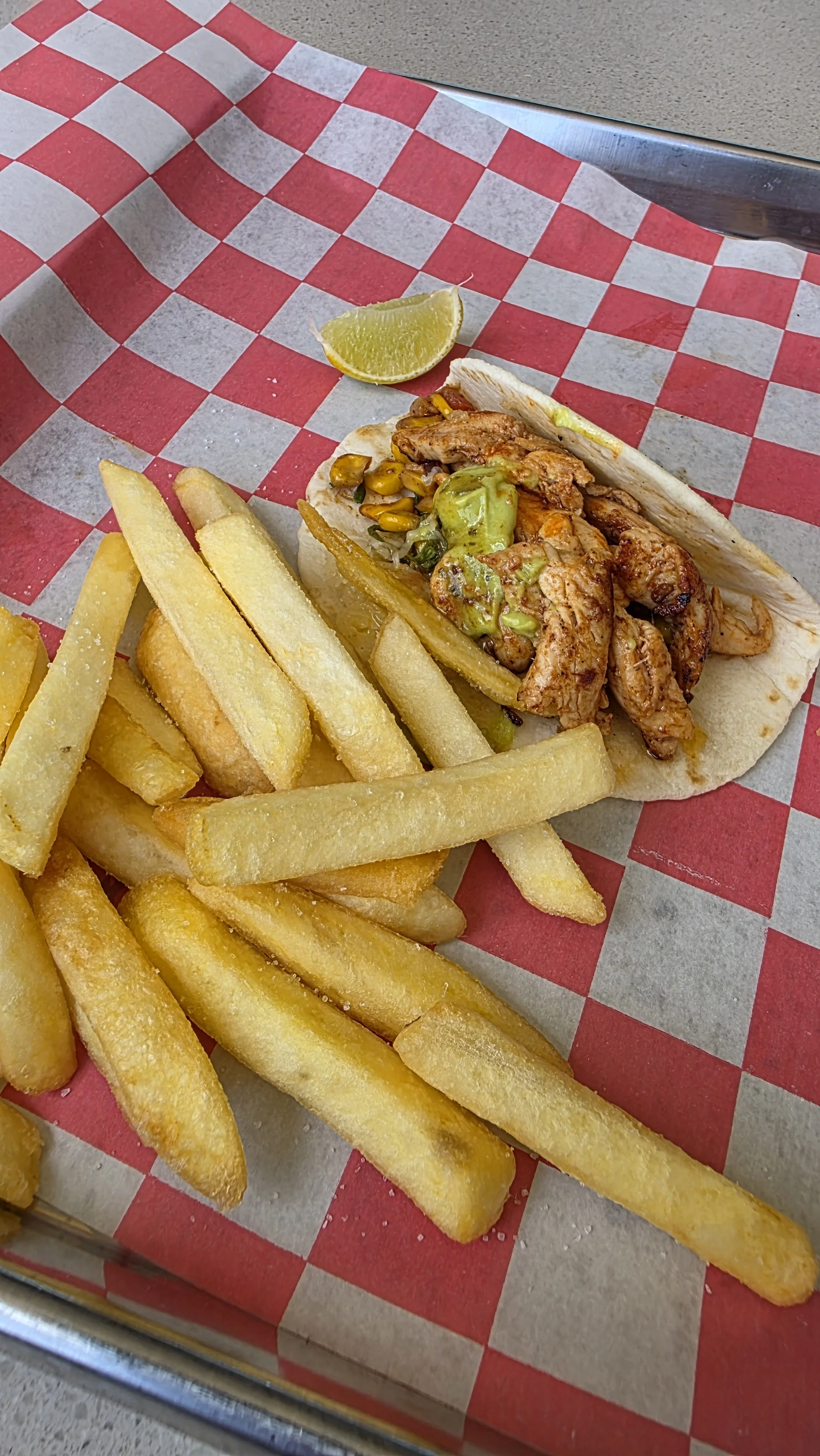 French fries and a taco with grilled chicken, vegetables, and sauce on red and white checkered paper