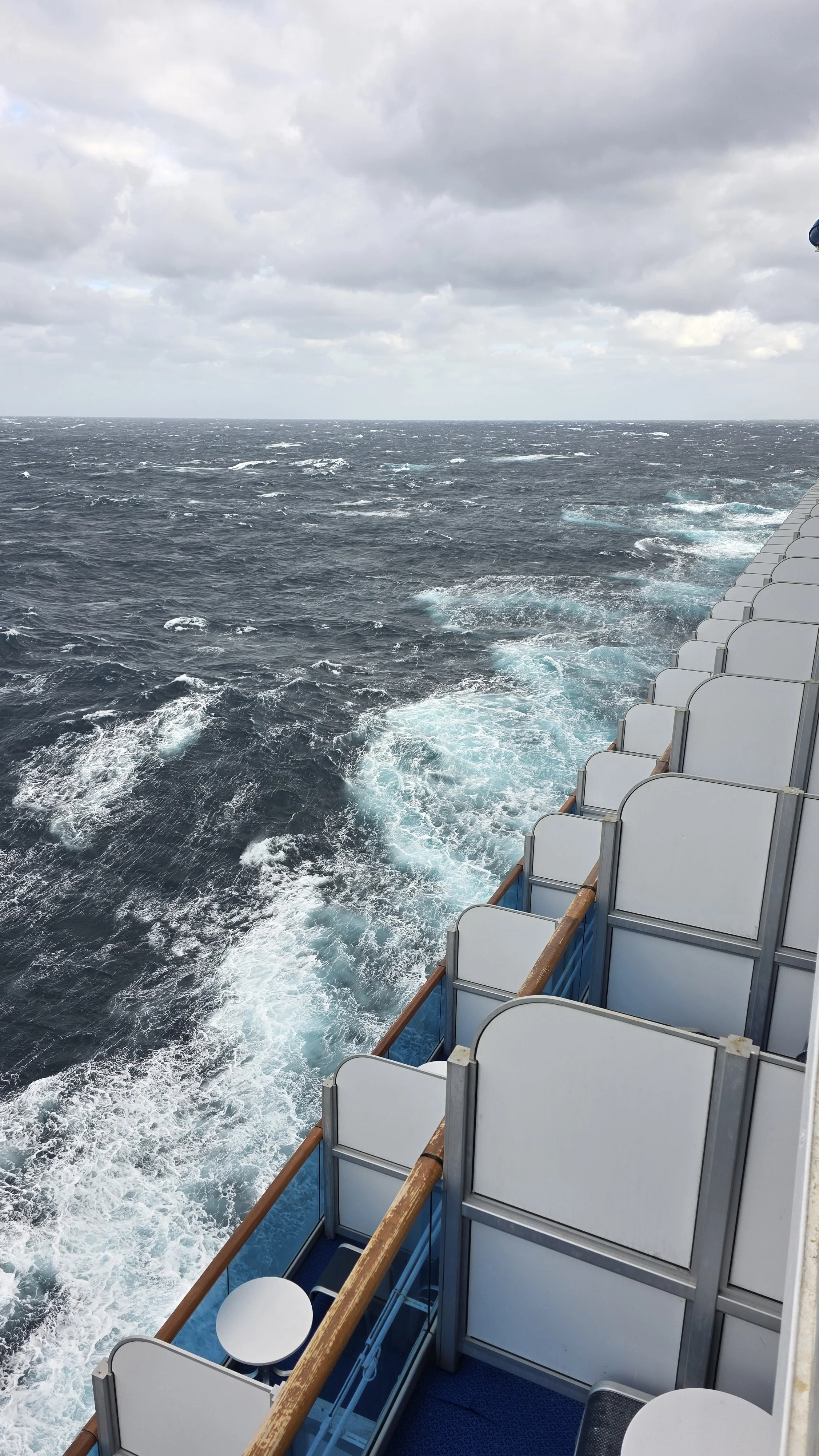 View from a cruise ship deck showing the ocean and a cloudy sky.